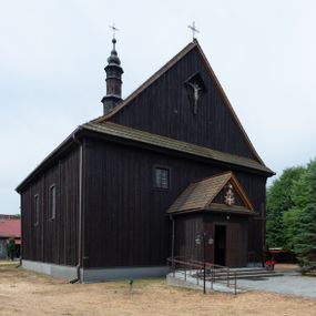 Zdjęcie nr 1: Kościół z drewna modrzewiowego o konstrukcji zrębowej, na betonowej podmurówce, otoczony drewnianym ogrodzeniem. Bryła składa się z korpusu nawowego na planie prostokąta oraz z wydłużonego, prostokątnego prezbiterium z zakrystią na przedłużeniu, węższego od nawy, zakończonego ścianą prostą, skierowanego na południe. Od strony północnej dobudowana jest prostokątna kruchta, od zachodu dwa przedsionki na dwóch skrajnych bokach –  przy nawie i prezbiterium. 
Trójprzęsłowe prezbiterium nakryte jest  sklepieniem pozornym zwierciadlanym, które przedłuża się nad nawę środkową. Ściany prezbiterium artykułowane pilastrami dzielą je na trzy przęsła. Kapitele pilastrów dźwigają nasadniki, które podtrzymują gzymsik. Przedłużeniem kapiteli w strefie stropu są płaskie belki biegnące przez całą jego szerokość, wyznaczając tym samym pola, w których umieszczono polichromię. Po obu stronach ołtarza drzwi w kształcie stojącego prostokąta. Prezbiterium od korpusu nawowego oddzielone silnie wystającą belką sklepienia oraz belką tęczową z grupą Ukrzyżowania. 
Korpus o trzech nawach o układzie halowym, z których środkowa jest dwa razy szersza od bocznych, trójprzęsłowa, z nawami oddzielonymi kanelowanymi filarami z nasadnikami podtrzymującymi gzyms. Nawy boczne nakryte kolebką. Na linii filarów pilastry na ścianach, łączą je poprzeczne belki sklepienia. W ostatnim przęśle chór muzyczny wsparty na dwóch filarach, z pełnym parapetem występującym w części środkowej trójbocznie do przodu. Jego krawędź dolna dekorowana jest lambrekinem. Ściany kościoła pokryte polichormią, pomalowane na jasnożółto, z jasnozielonymi podporami i brązowymi liniami podziału stropu. Te elementy wyznaczają ramy wypełnione polami z dekoracją ornamentalną w kształcie prostokątów i scenami figuralnymi zamkniętymi w kołach. 
Otwory okienne w drugim i trzecim przęśle nawy, od wschodu i zachodu, prostokątne. Także w prezbiterium po jednym prostokątnym oknie z każdej strony. Od strony wejścia dwa niewielkie okna prostokątne ponad kruchtą. Na ścianie zamknięcia zakrystii cztery prostokątne, symetrycznie rozłożone okna. 
 Fasada poprzedzona przedsionkiem w kształcie prostopadłościanu nakrytego dachem dwuspadowym, z przyczółkiem. Otwór drzwiowy w formie stojącego prostokąta, a w szczycie przyczółka trójkątne, wielodzielne okienko. Fasada w kształcie leżącego prostokąta z trójkątnym szczytem, części oddzielone daszkiem pulpitowym. Po dwóch stronach przedsionka prostokątne okna, w szczycie fasady  nakryty daszkiem krucyfiks. 
Elewacje zewnętrzne na podmurówce, artykułowane jedynie pionowymi, wystającymi przed lico belkami, przeprute oknami. Nad nawą i prezbiterium dachy dwuspadowe, nad prezbiterium niższy niż nad nawą, kryty blachą. Nad nawą wieżyczka na sygnaturkę zwieńczona cebulastym hełmem i krzyżem na szczycie. Na końcach dachu przy prezbiterium i nawie metalowe krzyże. 
