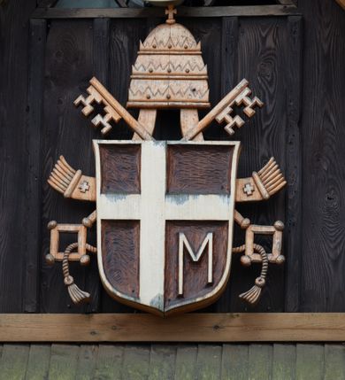 Zdjęcie nr 9: Kościół z drewna modrzewiowego o konstrukcji zrębowej, na betonowej podmurówce, otoczony drewnianym ogrodzeniem. Bryła składa się z korpusu nawowego na planie prostokąta oraz z wydłużonego, prostokątnego prezbiterium z zakrystią na przedłużeniu, węższego od nawy, zakończonego ścianą prostą, skierowanego na południe. Od strony północnej dobudowana jest prostokątna kruchta, od zachodu dwa przedsionki na dwóch skrajnych bokach –  przy nawie i prezbiterium. 
Trójprzęsłowe prezbiterium nakryte jest  sklepieniem pozornym zwierciadlanym, które przedłuża się nad nawę środkową. Ściany prezbiterium artykułowane pilastrami dzielą je na trzy przęsła. Kapitele pilastrów dźwigają nasadniki, które podtrzymują gzymsik. Przedłużeniem kapiteli w strefie stropu są płaskie belki biegnące przez całą jego szerokość, wyznaczając tym samym pola, w których umieszczono polichromię. Po obu stronach ołtarza drzwi w kształcie stojącego prostokąta. Prezbiterium od korpusu nawowego oddzielone silnie wystającą belką sklepienia oraz belką tęczową z grupą Ukrzyżowania. 
Korpus o trzech nawach o układzie halowym, z których środkowa jest dwa razy szersza od bocznych, trójprzęsłowa, z nawami oddzielonymi kanelowanymi filarami z nasadnikami podtrzymującymi gzyms. Nawy boczne nakryte kolebką. Na linii filarów pilastry na ścianach, łączą je poprzeczne belki sklepienia. W ostatnim przęśle chór muzyczny wsparty na dwóch filarach, z pełnym parapetem występującym w części środkowej trójbocznie do przodu. Jego krawędź dolna dekorowana jest lambrekinem. Ściany kościoła pokryte polichormią, pomalowane na jasnożółto, z jasnozielonymi podporami i brązowymi liniami podziału stropu. Te elementy wyznaczają ramy wypełnione polami z dekoracją ornamentalną w kształcie prostokątów i scenami figuralnymi zamkniętymi w kołach. 
Otwory okienne w drugim i trzecim przęśle nawy, od wschodu i zachodu, prostokątne. Także w prezbiterium po jednym prostokątnym oknie z każdej strony. Od strony wejścia dwa niewielkie okna prostokątne ponad kruchtą. Na ścianie zamknięcia zakrystii cztery prostokątne, symetrycznie rozłożone okna. 
 Fasada poprzedzona przedsionkiem w kształcie prostopadłościanu nakrytego dachem dwuspadowym, z przyczółkiem. Otwór drzwiowy w formie stojącego prostokąta, a w szczycie przyczółka trójkątne, wielodzielne okienko. Fasada w kształcie leżącego prostokąta z trójkątnym szczytem, części oddzielone daszkiem pulpitowym. Po dwóch stronach przedsionka prostokątne okna, w szczycie fasady  nakryty daszkiem krucyfiks. 
Elewacje zewnętrzne na podmurówce, artykułowane jedynie pionowymi, wystającymi przed lico belkami, przeprute oknami. Nad nawą i prezbiterium dachy dwuspadowe, nad prezbiterium niższy niż nad nawą, kryty blachą. Nad nawą wieżyczka na sygnaturkę zwieńczona cebulastym hełmem i krzyżem na szczycie. Na końcach dachu przy prezbiterium i nawie metalowe krzyże. 
