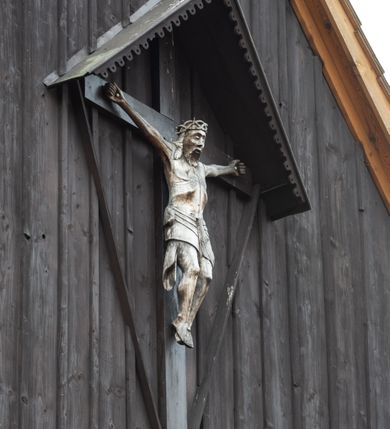 Zdjęcie nr 8: Kościół z drewna modrzewiowego o konstrukcji zrębowej, na betonowej podmurówce, otoczony drewnianym ogrodzeniem. Bryła składa się z korpusu nawowego na planie prostokąta oraz z wydłużonego, prostokątnego prezbiterium z zakrystią na przedłużeniu, węższego od nawy, zakończonego ścianą prostą, skierowanego na południe. Od strony północnej dobudowana jest prostokątna kruchta, od zachodu dwa przedsionki na dwóch skrajnych bokach –  przy nawie i prezbiterium. 
Trójprzęsłowe prezbiterium nakryte jest  sklepieniem pozornym zwierciadlanym, które przedłuża się nad nawę środkową. Ściany prezbiterium artykułowane pilastrami dzielą je na trzy przęsła. Kapitele pilastrów dźwigają nasadniki, które podtrzymują gzymsik. Przedłużeniem kapiteli w strefie stropu są płaskie belki biegnące przez całą jego szerokość, wyznaczając tym samym pola, w których umieszczono polichromię. Po obu stronach ołtarza drzwi w kształcie stojącego prostokąta. Prezbiterium od korpusu nawowego oddzielone silnie wystającą belką sklepienia oraz belką tęczową z grupą Ukrzyżowania. 
Korpus o trzech nawach o układzie halowym, z których środkowa jest dwa razy szersza od bocznych, trójprzęsłowa, z nawami oddzielonymi kanelowanymi filarami z nasadnikami podtrzymującymi gzyms. Nawy boczne nakryte kolebką. Na linii filarów pilastry na ścianach, łączą je poprzeczne belki sklepienia. W ostatnim przęśle chór muzyczny wsparty na dwóch filarach, z pełnym parapetem występującym w części środkowej trójbocznie do przodu. Jego krawędź dolna dekorowana jest lambrekinem. Ściany kościoła pokryte polichormią, pomalowane na jasnożółto, z jasnozielonymi podporami i brązowymi liniami podziału stropu. Te elementy wyznaczają ramy wypełnione polami z dekoracją ornamentalną w kształcie prostokątów i scenami figuralnymi zamkniętymi w kołach. 
Otwory okienne w drugim i trzecim przęśle nawy, od wschodu i zachodu, prostokątne. Także w prezbiterium po jednym prostokątnym oknie z każdej strony. Od strony wejścia dwa niewielkie okna prostokątne ponad kruchtą. Na ścianie zamknięcia zakrystii cztery prostokątne, symetrycznie rozłożone okna. 
 Fasada poprzedzona przedsionkiem w kształcie prostopadłościanu nakrytego dachem dwuspadowym, z przyczółkiem. Otwór drzwiowy w formie stojącego prostokąta, a w szczycie przyczółka trójkątne, wielodzielne okienko. Fasada w kształcie leżącego prostokąta z trójkątnym szczytem, części oddzielone daszkiem pulpitowym. Po dwóch stronach przedsionka prostokątne okna, w szczycie fasady  nakryty daszkiem krucyfiks. 
Elewacje zewnętrzne na podmurówce, artykułowane jedynie pionowymi, wystającymi przed lico belkami, przeprute oknami. Nad nawą i prezbiterium dachy dwuspadowe, nad prezbiterium niższy niż nad nawą, kryty blachą. Nad nawą wieżyczka na sygnaturkę zwieńczona cebulastym hełmem i krzyżem na szczycie. Na końcach dachu przy prezbiterium i nawie metalowe krzyże. 
