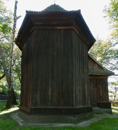 Zdjęcie nr 5: Kościół drewniany, orientowany, jednonawowy, wzniesiony na niewielkiej ceglanej podmurówce, o konstrukcji zrębowej, ściany szalowane pionowo z listowaniem, kruchta zachodnia o konstrukcji słupowo-ramowej. Nawa na rzucie prostokąta zbliżonego do kwadratu, prezbiterium węższe od nawy, wydłużone, zamknięte trójbocznie. Do północnej ściany prezbiterium przylega zakrystia na planie prostokąta. Do północnej ściany nawy przywiera niewielka kruchta na planie prostokąta, zamknięta trójbocznie. Przy zachodniej ścianie nawy znajduje się kruchta na rzucie prostokąta. Wnętrze nakryte pozornymi, spłaszczonymi sklepieniami o krzywiźnie przybierającej kształt łuku odcinkowego. Pomiędzy nawą a prezbiterium otwór tęczowy o wykroju prostokąta zbliżonego do kwadratu zamkniętego łukiem koszowym. Prezbiterium niższe od nawy, sięgające wysokości łuku tęczowego. Ściany prezbiterium i nawy obiega profilowany gzyms, oddzielający je od sklepień. W części zachodniej nawy parapet chóru muzycznego wsparty na dwóch kolumnach o stylizowanych kapitelach kompozytowych i kanelowanych trzonach na wysokich cokołach. W północno-zachodnim narożu drabiniaste schody prowadzące na chór w ośmiobocznej obudowie. Ściany i sklepienia pokryte polichromią. Na ścianach wzdłużnych oraz na osi ściany zachodniej otwory drzwiowe o prostokątnym wykroju zamknięte drzwiami spągowymi z desek oraz płycinowymi, na północnej ścianie prezbiterium prostokątny otwór drzwiowy do zakrystii. Posadzka z płyt kamiennych, szachownicowa. Kruchty i zakrystia nakryte stropami, przez nie dostęp do wnętrza. 
Elewacja frontowa jednoosiowa, zamknięta trójkątnym szczytem, poprzedzona kruchtą. Na osi wejście do kruchty zachodniej w postaci dwuskrzydłowych drzwi w formie stojącego prostokąta. Nad kruchtą pięterko dzwonowe z prostokątnym otworem zamykanym dwuskrzydłowymi okiennicami. Elewacja boczna południowa z czterema oknami, po dwa w nawie i prezbiterium. Elewacja północna przepruta dwoma oknami w części nawy. Okna krosnowe, w formie stojącego prostokąta, o niewielkich podziałach kwaterowych z witrażami. Na wschodniej ścianie kruchty północnej okno i jednoskrzydłowe drzwi. W zakrystii okno na ścianie północnej i drzwi jednoskrzydłowe na ścianie wschodniej. Kościół nakrywają dachy dwuspadowe, wyższy nad korpusem nawowym, niższy nad prezbiterium. Kruchta zachodnia w formie przysadzistej wieży, niższej od korpusu nawowego z pięterkiem dzwonowym, zwieńczonym hełmem baniastym, pokrytym gontem z iglicą oraz gałką i krzyżem. Kruchta północna z dachem wielospadowym. Zakrystia nakryta dachem pulpitowym. W połowie wysokości dachu znajduje się wieżyczka na sygnaturkę na ośmiobocznym obitym blachą trzonie, z ażurową latarnią nakrytą baniastym hełmem zakończonym kulą z krzyżem. 



