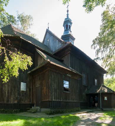 Zdjęcie nr 2: Kościół drewniany, orientowany, jednonawowy, wzniesiony na niewielkiej ceglanej podmurówce, o konstrukcji zrębowej, ściany szalowane pionowo z listowaniem, kruchta zachodnia o konstrukcji słupowo-ramowej. Nawa na rzucie prostokąta zbliżonego do kwadratu, prezbiterium węższe od nawy, wydłużone, zamknięte trójbocznie. Do północnej ściany prezbiterium przylega zakrystia na planie prostokąta. Do północnej ściany nawy przywiera niewielka kruchta na planie prostokąta, zamknięta trójbocznie. Przy zachodniej ścianie nawy znajduje się kruchta na rzucie prostokąta. Wnętrze nakryte pozornymi, spłaszczonymi sklepieniami o krzywiźnie przybierającej kształt łuku odcinkowego. Pomiędzy nawą a prezbiterium otwór tęczowy o wykroju prostokąta zbliżonego do kwadratu zamkniętego łukiem koszowym. Prezbiterium niższe od nawy, sięgające wysokości łuku tęczowego. Ściany prezbiterium i nawy obiega profilowany gzyms, oddzielający je od sklepień. W części zachodniej nawy parapet chóru muzycznego wsparty na dwóch kolumnach o stylizowanych kapitelach kompozytowych i kanelowanych trzonach na wysokich cokołach. W północno-zachodnim narożu drabiniaste schody prowadzące na chór w ośmiobocznej obudowie. Ściany i sklepienia pokryte polichromią. Na ścianach wzdłużnych oraz na osi ściany zachodniej otwory drzwiowe o prostokątnym wykroju zamknięte drzwiami spągowymi z desek oraz płycinowymi, na północnej ścianie prezbiterium prostokątny otwór drzwiowy do zakrystii. Posadzka z płyt kamiennych, szachownicowa. Kruchty i zakrystia nakryte stropami, przez nie dostęp do wnętrza. 
Elewacja frontowa jednoosiowa, zamknięta trójkątnym szczytem, poprzedzona kruchtą. Na osi wejście do kruchty zachodniej w postaci dwuskrzydłowych drzwi w formie stojącego prostokąta. Nad kruchtą pięterko dzwonowe z prostokątnym otworem zamykanym dwuskrzydłowymi okiennicami. Elewacja boczna południowa z czterema oknami, po dwa w nawie i prezbiterium. Elewacja północna przepruta dwoma oknami w części nawy. Okna krosnowe, w formie stojącego prostokąta, o niewielkich podziałach kwaterowych z witrażami. Na wschodniej ścianie kruchty północnej okno i jednoskrzydłowe drzwi. W zakrystii okno na ścianie północnej i drzwi jednoskrzydłowe na ścianie wschodniej. Kościół nakrywają dachy dwuspadowe, wyższy nad korpusem nawowym, niższy nad prezbiterium. Kruchta zachodnia w formie przysadzistej wieży, niższej od korpusu nawowego z pięterkiem dzwonowym, zwieńczonym hełmem baniastym, pokrytym gontem z iglicą oraz gałką i krzyżem. Kruchta północna z dachem wielospadowym. Zakrystia nakryta dachem pulpitowym. W połowie wysokości dachu znajduje się wieżyczka na sygnaturkę na ośmiobocznym obitym blachą trzonie, z ażurową latarnią nakrytą baniastym hełmem zakończonym kulą z krzyżem. 



