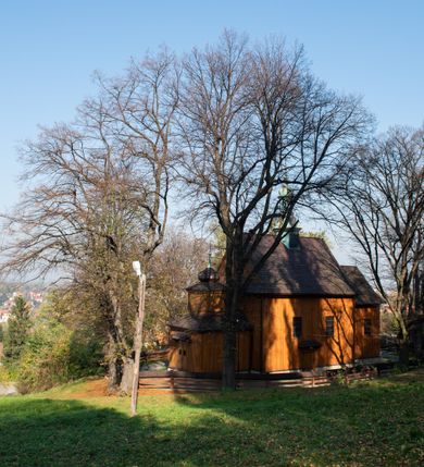 Zdjęcie nr 21: Kościół drewniany, orientowany, jednonawowy, wzniesiony na niewielkiej ceglanej podmurówce, o konstrukcji zrębowej, ściany szalowane pionowo z listowaniem, kruchta zachodnia o konstrukcji słupowo-ramowej. Nawa na rzucie prostokąta zbliżonego do kwadratu, prezbiterium węższe od nawy, wydłużone, zamknięte trójbocznie. Do północnej ściany prezbiterium przylega zakrystia na planie prostokąta. Do północnej ściany nawy przywiera niewielka kruchta na planie prostokąta, zamknięta trójbocznie. Przy zachodniej ścianie nawy znajduje się kruchta na rzucie prostokąta. Wnętrze nakryte pozornymi, spłaszczonymi sklepieniami o krzywiźnie przybierającej kształt łuku odcinkowego. Pomiędzy nawą a prezbiterium otwór tęczowy o wykroju prostokąta zbliżonego do kwadratu zamkniętego łukiem koszowym. Prezbiterium niższe od nawy, sięgające wysokości łuku tęczowego. Ściany prezbiterium i nawy obiega profilowany gzyms, oddzielający je od sklepień. W części zachodniej nawy parapet chóru muzycznego wsparty na dwóch kolumnach o stylizowanych kapitelach kompozytowych i kanelowanych trzonach na wysokich cokołach. W północno-zachodnim narożu drabiniaste schody prowadzące na chór w ośmiobocznej obudowie. Ściany i sklepienia pokryte polichromią. Na ścianach wzdłużnych oraz na osi ściany zachodniej otwory drzwiowe o prostokątnym wykroju zamknięte drzwiami spągowymi z desek oraz płycinowymi, na północnej ścianie prezbiterium prostokątny otwór drzwiowy do zakrystii. Posadzka z płyt kamiennych, szachownicowa. Kruchty i zakrystia nakryte stropami, przez nie dostęp do wnętrza. 
Elewacja frontowa jednoosiowa, zamknięta trójkątnym szczytem, poprzedzona kruchtą. Na osi wejście do kruchty zachodniej w postaci dwuskrzydłowych drzwi w formie stojącego prostokąta. Nad kruchtą pięterko dzwonowe z prostokątnym otworem zamykanym dwuskrzydłowymi okiennicami. Elewacja boczna południowa z czterema oknami, po dwa w nawie i prezbiterium. Elewacja północna przepruta dwoma oknami w części nawy. Okna krosnowe, w formie stojącego prostokąta, o niewielkich podziałach kwaterowych z witrażami. Na wschodniej ścianie kruchty północnej okno i jednoskrzydłowe drzwi. W zakrystii okno na ścianie północnej i drzwi jednoskrzydłowe na ścianie wschodniej. Kościół nakrywają dachy dwuspadowe, wyższy nad korpusem nawowym, niższy nad prezbiterium. Kruchta zachodnia w formie przysadzistej wieży, niższej od korpusu nawowego z pięterkiem dzwonowym, zwieńczonym hełmem baniastym, pokrytym gontem z iglicą oraz gałką i krzyżem. Kruchta północna z dachem wielospadowym. Zakrystia nakryta dachem pulpitowym. W połowie wysokości dachu znajduje się wieżyczka na sygnaturkę na ośmiobocznym obitym blachą trzonie, z ażurową latarnią nakrytą baniastym hełmem zakończonym kulą z krzyżem. 



