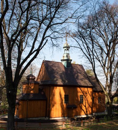 Zdjęcie nr 19: Kościół drewniany, orientowany, jednonawowy, wzniesiony na niewielkiej ceglanej podmurówce, o konstrukcji zrębowej, ściany szalowane pionowo z listowaniem, kruchta zachodnia o konstrukcji słupowo-ramowej. Nawa na rzucie prostokąta zbliżonego do kwadratu, prezbiterium węższe od nawy, wydłużone, zamknięte trójbocznie. Do północnej ściany prezbiterium przylega zakrystia na planie prostokąta. Do północnej ściany nawy przywiera niewielka kruchta na planie prostokąta, zamknięta trójbocznie. Przy zachodniej ścianie nawy znajduje się kruchta na rzucie prostokąta. Wnętrze nakryte pozornymi, spłaszczonymi sklepieniami o krzywiźnie przybierającej kształt łuku odcinkowego. Pomiędzy nawą a prezbiterium otwór tęczowy o wykroju prostokąta zbliżonego do kwadratu zamkniętego łukiem koszowym. Prezbiterium niższe od nawy, sięgające wysokości łuku tęczowego. Ściany prezbiterium i nawy obiega profilowany gzyms, oddzielający je od sklepień. W części zachodniej nawy parapet chóru muzycznego wsparty na dwóch kolumnach o stylizowanych kapitelach kompozytowych i kanelowanych trzonach na wysokich cokołach. W północno-zachodnim narożu drabiniaste schody prowadzące na chór w ośmiobocznej obudowie. Ściany i sklepienia pokryte polichromią. Na ścianach wzdłużnych oraz na osi ściany zachodniej otwory drzwiowe o prostokątnym wykroju zamknięte drzwiami spągowymi z desek oraz płycinowymi, na północnej ścianie prezbiterium prostokątny otwór drzwiowy do zakrystii. Posadzka z płyt kamiennych, szachownicowa. Kruchty i zakrystia nakryte stropami, przez nie dostęp do wnętrza. 
Elewacja frontowa jednoosiowa, zamknięta trójkątnym szczytem, poprzedzona kruchtą. Na osi wejście do kruchty zachodniej w postaci dwuskrzydłowych drzwi w formie stojącego prostokąta. Nad kruchtą pięterko dzwonowe z prostokątnym otworem zamykanym dwuskrzydłowymi okiennicami. Elewacja boczna południowa z czterema oknami, po dwa w nawie i prezbiterium. Elewacja północna przepruta dwoma oknami w części nawy. Okna krosnowe, w formie stojącego prostokąta, o niewielkich podziałach kwaterowych z witrażami. Na wschodniej ścianie kruchty północnej okno i jednoskrzydłowe drzwi. W zakrystii okno na ścianie północnej i drzwi jednoskrzydłowe na ścianie wschodniej. Kościół nakrywają dachy dwuspadowe, wyższy nad korpusem nawowym, niższy nad prezbiterium. Kruchta zachodnia w formie przysadzistej wieży, niższej od korpusu nawowego z pięterkiem dzwonowym, zwieńczonym hełmem baniastym, pokrytym gontem z iglicą oraz gałką i krzyżem. Kruchta północna z dachem wielospadowym. Zakrystia nakryta dachem pulpitowym. W połowie wysokości dachu znajduje się wieżyczka na sygnaturkę na ośmiobocznym obitym blachą trzonie, z ażurową latarnią nakrytą baniastym hełmem zakończonym kulą z krzyżem. 



