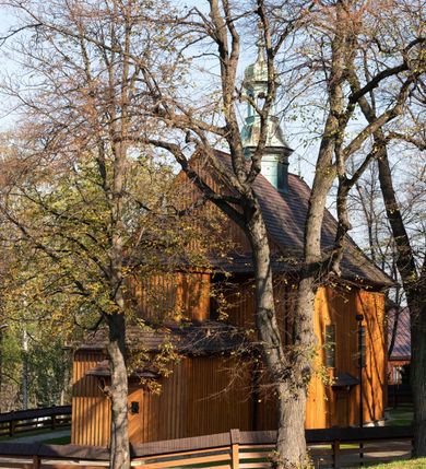 Zdjęcie nr 24: Kościół drewniany, orientowany, jednonawowy, wzniesiony na niewielkiej ceglanej podmurówce, o konstrukcji zrębowej, ściany szalowane pionowo z listowaniem, kruchta zachodnia o konstrukcji słupowo-ramowej. Nawa na rzucie prostokąta zbliżonego do kwadratu, prezbiterium węższe od nawy, wydłużone, zamknięte trójbocznie. Do północnej ściany prezbiterium przylega zakrystia na planie prostokąta. Do północnej ściany nawy przywiera niewielka kruchta na planie prostokąta, zamknięta trójbocznie. Przy zachodniej ścianie nawy znajduje się kruchta na rzucie prostokąta. Wnętrze nakryte pozornymi, spłaszczonymi sklepieniami o krzywiźnie przybierającej kształt łuku odcinkowego. Pomiędzy nawą a prezbiterium otwór tęczowy o wykroju prostokąta zbliżonego do kwadratu zamkniętego łukiem koszowym. Prezbiterium niższe od nawy, sięgające wysokości łuku tęczowego. Ściany prezbiterium i nawy obiega profilowany gzyms, oddzielający je od sklepień. W części zachodniej nawy parapet chóru muzycznego wsparty na dwóch kolumnach o stylizowanych kapitelach kompozytowych i kanelowanych trzonach na wysokich cokołach. W północno-zachodnim narożu drabiniaste schody prowadzące na chór w ośmiobocznej obudowie. Ściany i sklepienia pokryte polichromią. Na ścianach wzdłużnych oraz na osi ściany zachodniej otwory drzwiowe o prostokątnym wykroju zamknięte drzwiami spągowymi z desek oraz płycinowymi, na północnej ścianie prezbiterium prostokątny otwór drzwiowy do zakrystii. Posadzka z płyt kamiennych, szachownicowa. Kruchty i zakrystia nakryte stropami, przez nie dostęp do wnętrza. 
Elewacja frontowa jednoosiowa, zamknięta trójkątnym szczytem, poprzedzona kruchtą. Na osi wejście do kruchty zachodniej w postaci dwuskrzydłowych drzwi w formie stojącego prostokąta. Nad kruchtą pięterko dzwonowe z prostokątnym otworem zamykanym dwuskrzydłowymi okiennicami. Elewacja boczna południowa z czterema oknami, po dwa w nawie i prezbiterium. Elewacja północna przepruta dwoma oknami w części nawy. Okna krosnowe, w formie stojącego prostokąta, o niewielkich podziałach kwaterowych z witrażami. Na wschodniej ścianie kruchty północnej okno i jednoskrzydłowe drzwi. W zakrystii okno na ścianie północnej i drzwi jednoskrzydłowe na ścianie wschodniej. Kościół nakrywają dachy dwuspadowe, wyższy nad korpusem nawowym, niższy nad prezbiterium. Kruchta zachodnia w formie przysadzistej wieży, niższej od korpusu nawowego z pięterkiem dzwonowym, zwieńczonym hełmem baniastym, pokrytym gontem z iglicą oraz gałką i krzyżem. Kruchta północna z dachem wielospadowym. Zakrystia nakryta dachem pulpitowym. W połowie wysokości dachu znajduje się wieżyczka na sygnaturkę na ośmiobocznym obitym blachą trzonie, z ażurową latarnią nakrytą baniastym hełmem zakończonym kulą z krzyżem. 



