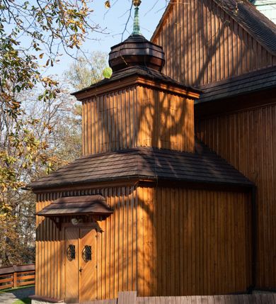 Zdjęcie nr 31: Kościół drewniany, orientowany, jednonawowy, wzniesiony na niewielkiej ceglanej podmurówce, o konstrukcji zrębowej, ściany szalowane pionowo z listowaniem, kruchta zachodnia o konstrukcji słupowo-ramowej. Nawa na rzucie prostokąta zbliżonego do kwadratu, prezbiterium węższe od nawy, wydłużone, zamknięte trójbocznie. Do północnej ściany prezbiterium przylega zakrystia na planie prostokąta. Do północnej ściany nawy przywiera niewielka kruchta na planie prostokąta, zamknięta trójbocznie. Przy zachodniej ścianie nawy znajduje się kruchta na rzucie prostokąta. Wnętrze nakryte pozornymi, spłaszczonymi sklepieniami o krzywiźnie przybierającej kształt łuku odcinkowego. Pomiędzy nawą a prezbiterium otwór tęczowy o wykroju prostokąta zbliżonego do kwadratu zamkniętego łukiem koszowym. Prezbiterium niższe od nawy, sięgające wysokości łuku tęczowego. Ściany prezbiterium i nawy obiega profilowany gzyms, oddzielający je od sklepień. W części zachodniej nawy parapet chóru muzycznego wsparty na dwóch kolumnach o stylizowanych kapitelach kompozytowych i kanelowanych trzonach na wysokich cokołach. W północno-zachodnim narożu drabiniaste schody prowadzące na chór w ośmiobocznej obudowie. Ściany i sklepienia pokryte polichromią. Na ścianach wzdłużnych oraz na osi ściany zachodniej otwory drzwiowe o prostokątnym wykroju zamknięte drzwiami spągowymi z desek oraz płycinowymi, na północnej ścianie prezbiterium prostokątny otwór drzwiowy do zakrystii. Posadzka z płyt kamiennych, szachownicowa. Kruchty i zakrystia nakryte stropami, przez nie dostęp do wnętrza. 
Elewacja frontowa jednoosiowa, zamknięta trójkątnym szczytem, poprzedzona kruchtą. Na osi wejście do kruchty zachodniej w postaci dwuskrzydłowych drzwi w formie stojącego prostokąta. Nad kruchtą pięterko dzwonowe z prostokątnym otworem zamykanym dwuskrzydłowymi okiennicami. Elewacja boczna południowa z czterema oknami, po dwa w nawie i prezbiterium. Elewacja północna przepruta dwoma oknami w części nawy. Okna krosnowe, w formie stojącego prostokąta, o niewielkich podziałach kwaterowych z witrażami. Na wschodniej ścianie kruchty północnej okno i jednoskrzydłowe drzwi. W zakrystii okno na ścianie północnej i drzwi jednoskrzydłowe na ścianie wschodniej. Kościół nakrywają dachy dwuspadowe, wyższy nad korpusem nawowym, niższy nad prezbiterium. Kruchta zachodnia w formie przysadzistej wieży, niższej od korpusu nawowego z pięterkiem dzwonowym, zwieńczonym hełmem baniastym, pokrytym gontem z iglicą oraz gałką i krzyżem. Kruchta północna z dachem wielospadowym. Zakrystia nakryta dachem pulpitowym. W połowie wysokości dachu znajduje się wieżyczka na sygnaturkę na ośmiobocznym obitym blachą trzonie, z ażurową latarnią nakrytą baniastym hełmem zakończonym kulą z krzyżem. 



