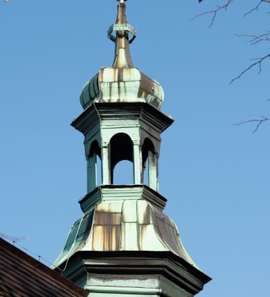 Zdjęcie nr 32: Kościół drewniany, orientowany, jednonawowy, wzniesiony na niewielkiej ceglanej podmurówce, o konstrukcji zrębowej, ściany szalowane pionowo z listowaniem, kruchta zachodnia o konstrukcji słupowo-ramowej. Nawa na rzucie prostokąta zbliżonego do kwadratu, prezbiterium węższe od nawy, wydłużone, zamknięte trójbocznie. Do północnej ściany prezbiterium przylega zakrystia na planie prostokąta. Do północnej ściany nawy przywiera niewielka kruchta na planie prostokąta, zamknięta trójbocznie. Przy zachodniej ścianie nawy znajduje się kruchta na rzucie prostokąta. Wnętrze nakryte pozornymi, spłaszczonymi sklepieniami o krzywiźnie przybierającej kształt łuku odcinkowego. Pomiędzy nawą a prezbiterium otwór tęczowy o wykroju prostokąta zbliżonego do kwadratu zamkniętego łukiem koszowym. Prezbiterium niższe od nawy, sięgające wysokości łuku tęczowego. Ściany prezbiterium i nawy obiega profilowany gzyms, oddzielający je od sklepień. W części zachodniej nawy parapet chóru muzycznego wsparty na dwóch kolumnach o stylizowanych kapitelach kompozytowych i kanelowanych trzonach na wysokich cokołach. W północno-zachodnim narożu drabiniaste schody prowadzące na chór w ośmiobocznej obudowie. Ściany i sklepienia pokryte polichromią. Na ścianach wzdłużnych oraz na osi ściany zachodniej otwory drzwiowe o prostokątnym wykroju zamknięte drzwiami spągowymi z desek oraz płycinowymi, na północnej ścianie prezbiterium prostokątny otwór drzwiowy do zakrystii. Posadzka z płyt kamiennych, szachownicowa. Kruchty i zakrystia nakryte stropami, przez nie dostęp do wnętrza. 
Elewacja frontowa jednoosiowa, zamknięta trójkątnym szczytem, poprzedzona kruchtą. Na osi wejście do kruchty zachodniej w postaci dwuskrzydłowych drzwi w formie stojącego prostokąta. Nad kruchtą pięterko dzwonowe z prostokątnym otworem zamykanym dwuskrzydłowymi okiennicami. Elewacja boczna południowa z czterema oknami, po dwa w nawie i prezbiterium. Elewacja północna przepruta dwoma oknami w części nawy. Okna krosnowe, w formie stojącego prostokąta, o niewielkich podziałach kwaterowych z witrażami. Na wschodniej ścianie kruchty północnej okno i jednoskrzydłowe drzwi. W zakrystii okno na ścianie północnej i drzwi jednoskrzydłowe na ścianie wschodniej. Kościół nakrywają dachy dwuspadowe, wyższy nad korpusem nawowym, niższy nad prezbiterium. Kruchta zachodnia w formie przysadzistej wieży, niższej od korpusu nawowego z pięterkiem dzwonowym, zwieńczonym hełmem baniastym, pokrytym gontem z iglicą oraz gałką i krzyżem. Kruchta północna z dachem wielospadowym. Zakrystia nakryta dachem pulpitowym. W połowie wysokości dachu znajduje się wieżyczka na sygnaturkę na ośmiobocznym obitym blachą trzonie, z ażurową latarnią nakrytą baniastym hełmem zakończonym kulą z krzyżem. 



