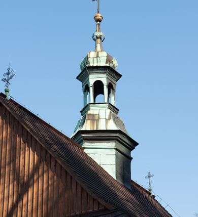 Zdjęcie nr 33: Kościół drewniany, orientowany, jednonawowy, wzniesiony na niewielkiej ceglanej podmurówce, o konstrukcji zrębowej, ściany szalowane pionowo z listowaniem, kruchta zachodnia o konstrukcji słupowo-ramowej. Nawa na rzucie prostokąta zbliżonego do kwadratu, prezbiterium węższe od nawy, wydłużone, zamknięte trójbocznie. Do północnej ściany prezbiterium przylega zakrystia na planie prostokąta. Do północnej ściany nawy przywiera niewielka kruchta na planie prostokąta, zamknięta trójbocznie. Przy zachodniej ścianie nawy znajduje się kruchta na rzucie prostokąta. Wnętrze nakryte pozornymi, spłaszczonymi sklepieniami o krzywiźnie przybierającej kształt łuku odcinkowego. Pomiędzy nawą a prezbiterium otwór tęczowy o wykroju prostokąta zbliżonego do kwadratu zamkniętego łukiem koszowym. Prezbiterium niższe od nawy, sięgające wysokości łuku tęczowego. Ściany prezbiterium i nawy obiega profilowany gzyms, oddzielający je od sklepień. W części zachodniej nawy parapet chóru muzycznego wsparty na dwóch kolumnach o stylizowanych kapitelach kompozytowych i kanelowanych trzonach na wysokich cokołach. W północno-zachodnim narożu drabiniaste schody prowadzące na chór w ośmiobocznej obudowie. Ściany i sklepienia pokryte polichromią. Na ścianach wzdłużnych oraz na osi ściany zachodniej otwory drzwiowe o prostokątnym wykroju zamknięte drzwiami spągowymi z desek oraz płycinowymi, na północnej ścianie prezbiterium prostokątny otwór drzwiowy do zakrystii. Posadzka z płyt kamiennych, szachownicowa. Kruchty i zakrystia nakryte stropami, przez nie dostęp do wnętrza. 
Elewacja frontowa jednoosiowa, zamknięta trójkątnym szczytem, poprzedzona kruchtą. Na osi wejście do kruchty zachodniej w postaci dwuskrzydłowych drzwi w formie stojącego prostokąta. Nad kruchtą pięterko dzwonowe z prostokątnym otworem zamykanym dwuskrzydłowymi okiennicami. Elewacja boczna południowa z czterema oknami, po dwa w nawie i prezbiterium. Elewacja północna przepruta dwoma oknami w części nawy. Okna krosnowe, w formie stojącego prostokąta, o niewielkich podziałach kwaterowych z witrażami. Na wschodniej ścianie kruchty północnej okno i jednoskrzydłowe drzwi. W zakrystii okno na ścianie północnej i drzwi jednoskrzydłowe na ścianie wschodniej. Kościół nakrywają dachy dwuspadowe, wyższy nad korpusem nawowym, niższy nad prezbiterium. Kruchta zachodnia w formie przysadzistej wieży, niższej od korpusu nawowego z pięterkiem dzwonowym, zwieńczonym hełmem baniastym, pokrytym gontem z iglicą oraz gałką i krzyżem. Kruchta północna z dachem wielospadowym. Zakrystia nakryta dachem pulpitowym. W połowie wysokości dachu znajduje się wieżyczka na sygnaturkę na ośmiobocznym obitym blachą trzonie, z ażurową latarnią nakrytą baniastym hełmem zakończonym kulą z krzyżem. 



