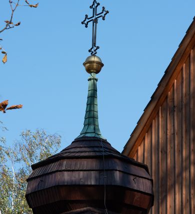 Zdjęcie nr 35: Kościół drewniany, orientowany, jednonawowy, wzniesiony na niewielkiej ceglanej podmurówce, o konstrukcji zrębowej, ściany szalowane pionowo z listowaniem, kruchta zachodnia o konstrukcji słupowo-ramowej. Nawa na rzucie prostokąta zbliżonego do kwadratu, prezbiterium węższe od nawy, wydłużone, zamknięte trójbocznie. Do północnej ściany prezbiterium przylega zakrystia na planie prostokąta. Do północnej ściany nawy przywiera niewielka kruchta na planie prostokąta, zamknięta trójbocznie. Przy zachodniej ścianie nawy znajduje się kruchta na rzucie prostokąta. Wnętrze nakryte pozornymi, spłaszczonymi sklepieniami o krzywiźnie przybierającej kształt łuku odcinkowego. Pomiędzy nawą a prezbiterium otwór tęczowy o wykroju prostokąta zbliżonego do kwadratu zamkniętego łukiem koszowym. Prezbiterium niższe od nawy, sięgające wysokości łuku tęczowego. Ściany prezbiterium i nawy obiega profilowany gzyms, oddzielający je od sklepień. W części zachodniej nawy parapet chóru muzycznego wsparty na dwóch kolumnach o stylizowanych kapitelach kompozytowych i kanelowanych trzonach na wysokich cokołach. W północno-zachodnim narożu drabiniaste schody prowadzące na chór w ośmiobocznej obudowie. Ściany i sklepienia pokryte polichromią. Na ścianach wzdłużnych oraz na osi ściany zachodniej otwory drzwiowe o prostokątnym wykroju zamknięte drzwiami spągowymi z desek oraz płycinowymi, na północnej ścianie prezbiterium prostokątny otwór drzwiowy do zakrystii. Posadzka z płyt kamiennych, szachownicowa. Kruchty i zakrystia nakryte stropami, przez nie dostęp do wnętrza. 
Elewacja frontowa jednoosiowa, zamknięta trójkątnym szczytem, poprzedzona kruchtą. Na osi wejście do kruchty zachodniej w postaci dwuskrzydłowych drzwi w formie stojącego prostokąta. Nad kruchtą pięterko dzwonowe z prostokątnym otworem zamykanym dwuskrzydłowymi okiennicami. Elewacja boczna południowa z czterema oknami, po dwa w nawie i prezbiterium. Elewacja północna przepruta dwoma oknami w części nawy. Okna krosnowe, w formie stojącego prostokąta, o niewielkich podziałach kwaterowych z witrażami. Na wschodniej ścianie kruchty północnej okno i jednoskrzydłowe drzwi. W zakrystii okno na ścianie północnej i drzwi jednoskrzydłowe na ścianie wschodniej. Kościół nakrywają dachy dwuspadowe, wyższy nad korpusem nawowym, niższy nad prezbiterium. Kruchta zachodnia w formie przysadzistej wieży, niższej od korpusu nawowego z pięterkiem dzwonowym, zwieńczonym hełmem baniastym, pokrytym gontem z iglicą oraz gałką i krzyżem. Kruchta północna z dachem wielospadowym. Zakrystia nakryta dachem pulpitowym. W połowie wysokości dachu znajduje się wieżyczka na sygnaturkę na ośmiobocznym obitym blachą trzonie, z ażurową latarnią nakrytą baniastym hełmem zakończonym kulą z krzyżem. 



