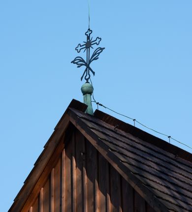 Zdjęcie nr 36: Kościół drewniany, orientowany, jednonawowy, wzniesiony na niewielkiej ceglanej podmurówce, o konstrukcji zrębowej, ściany szalowane pionowo z listowaniem, kruchta zachodnia o konstrukcji słupowo-ramowej. Nawa na rzucie prostokąta zbliżonego do kwadratu, prezbiterium węższe od nawy, wydłużone, zamknięte trójbocznie. Do północnej ściany prezbiterium przylega zakrystia na planie prostokąta. Do północnej ściany nawy przywiera niewielka kruchta na planie prostokąta, zamknięta trójbocznie. Przy zachodniej ścianie nawy znajduje się kruchta na rzucie prostokąta. Wnętrze nakryte pozornymi, spłaszczonymi sklepieniami o krzywiźnie przybierającej kształt łuku odcinkowego. Pomiędzy nawą a prezbiterium otwór tęczowy o wykroju prostokąta zbliżonego do kwadratu zamkniętego łukiem koszowym. Prezbiterium niższe od nawy, sięgające wysokości łuku tęczowego. Ściany prezbiterium i nawy obiega profilowany gzyms, oddzielający je od sklepień. W części zachodniej nawy parapet chóru muzycznego wsparty na dwóch kolumnach o stylizowanych kapitelach kompozytowych i kanelowanych trzonach na wysokich cokołach. W północno-zachodnim narożu drabiniaste schody prowadzące na chór w ośmiobocznej obudowie. Ściany i sklepienia pokryte polichromią. Na ścianach wzdłużnych oraz na osi ściany zachodniej otwory drzwiowe o prostokątnym wykroju zamknięte drzwiami spągowymi z desek oraz płycinowymi, na północnej ścianie prezbiterium prostokątny otwór drzwiowy do zakrystii. Posadzka z płyt kamiennych, szachownicowa. Kruchty i zakrystia nakryte stropami, przez nie dostęp do wnętrza. 
Elewacja frontowa jednoosiowa, zamknięta trójkątnym szczytem, poprzedzona kruchtą. Na osi wejście do kruchty zachodniej w postaci dwuskrzydłowych drzwi w formie stojącego prostokąta. Nad kruchtą pięterko dzwonowe z prostokątnym otworem zamykanym dwuskrzydłowymi okiennicami. Elewacja boczna południowa z czterema oknami, po dwa w nawie i prezbiterium. Elewacja północna przepruta dwoma oknami w części nawy. Okna krosnowe, w formie stojącego prostokąta, o niewielkich podziałach kwaterowych z witrażami. Na wschodniej ścianie kruchty północnej okno i jednoskrzydłowe drzwi. W zakrystii okno na ścianie północnej i drzwi jednoskrzydłowe na ścianie wschodniej. Kościół nakrywają dachy dwuspadowe, wyższy nad korpusem nawowym, niższy nad prezbiterium. Kruchta zachodnia w formie przysadzistej wieży, niższej od korpusu nawowego z pięterkiem dzwonowym, zwieńczonym hełmem baniastym, pokrytym gontem z iglicą oraz gałką i krzyżem. Kruchta północna z dachem wielospadowym. Zakrystia nakryta dachem pulpitowym. W połowie wysokości dachu znajduje się wieżyczka na sygnaturkę na ośmiobocznym obitym blachą trzonie, z ażurową latarnią nakrytą baniastym hełmem zakończonym kulą z krzyżem. 



