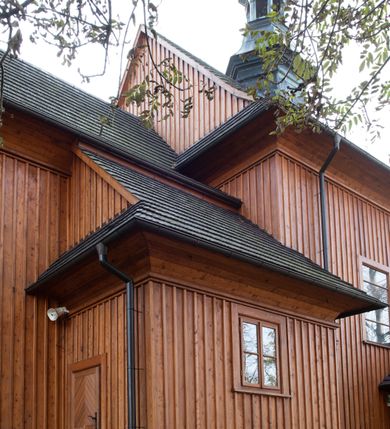 Zdjęcie nr 40: Kościół drewniany, orientowany, jednonawowy, wzniesiony na niewielkiej ceglanej podmurówce, o konstrukcji zrębowej, ściany szalowane pionowo z listowaniem, kruchta zachodnia o konstrukcji słupowo-ramowej. Nawa na rzucie prostokąta zbliżonego do kwadratu, prezbiterium węższe od nawy, wydłużone, zamknięte trójbocznie. Do północnej ściany prezbiterium przylega zakrystia na planie prostokąta. Do północnej ściany nawy przywiera niewielka kruchta na planie prostokąta, zamknięta trójbocznie. Przy zachodniej ścianie nawy znajduje się kruchta na rzucie prostokąta. Wnętrze nakryte pozornymi, spłaszczonymi sklepieniami o krzywiźnie przybierającej kształt łuku odcinkowego. Pomiędzy nawą a prezbiterium otwór tęczowy o wykroju prostokąta zbliżonego do kwadratu zamkniętego łukiem koszowym. Prezbiterium niższe od nawy, sięgające wysokości łuku tęczowego. Ściany prezbiterium i nawy obiega profilowany gzyms, oddzielający je od sklepień. W części zachodniej nawy parapet chóru muzycznego wsparty na dwóch kolumnach o stylizowanych kapitelach kompozytowych i kanelowanych trzonach na wysokich cokołach. W północno-zachodnim narożu drabiniaste schody prowadzące na chór w ośmiobocznej obudowie. Ściany i sklepienia pokryte polichromią. Na ścianach wzdłużnych oraz na osi ściany zachodniej otwory drzwiowe o prostokątnym wykroju zamknięte drzwiami spągowymi z desek oraz płycinowymi, na północnej ścianie prezbiterium prostokątny otwór drzwiowy do zakrystii. Posadzka z płyt kamiennych, szachownicowa. Kruchty i zakrystia nakryte stropami, przez nie dostęp do wnętrza. 
Elewacja frontowa jednoosiowa, zamknięta trójkątnym szczytem, poprzedzona kruchtą. Na osi wejście do kruchty zachodniej w postaci dwuskrzydłowych drzwi w formie stojącego prostokąta. Nad kruchtą pięterko dzwonowe z prostokątnym otworem zamykanym dwuskrzydłowymi okiennicami. Elewacja boczna południowa z czterema oknami, po dwa w nawie i prezbiterium. Elewacja północna przepruta dwoma oknami w części nawy. Okna krosnowe, w formie stojącego prostokąta, o niewielkich podziałach kwaterowych z witrażami. Na wschodniej ścianie kruchty północnej okno i jednoskrzydłowe drzwi. W zakrystii okno na ścianie północnej i drzwi jednoskrzydłowe na ścianie wschodniej. Kościół nakrywają dachy dwuspadowe, wyższy nad korpusem nawowym, niższy nad prezbiterium. Kruchta zachodnia w formie przysadzistej wieży, niższej od korpusu nawowego z pięterkiem dzwonowym, zwieńczonym hełmem baniastym, pokrytym gontem z iglicą oraz gałką i krzyżem. Kruchta północna z dachem wielospadowym. Zakrystia nakryta dachem pulpitowym. W połowie wysokości dachu znajduje się wieżyczka na sygnaturkę na ośmiobocznym obitym blachą trzonie, z ażurową latarnią nakrytą baniastym hełmem zakończonym kulą z krzyżem. 



