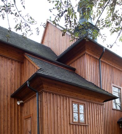 Zdjęcie nr 41: Kościół drewniany, orientowany, jednonawowy, wzniesiony na niewielkiej ceglanej podmurówce, o konstrukcji zrębowej, ściany szalowane pionowo z listowaniem, kruchta zachodnia o konstrukcji słupowo-ramowej. Nawa na rzucie prostokąta zbliżonego do kwadratu, prezbiterium węższe od nawy, wydłużone, zamknięte trójbocznie. Do północnej ściany prezbiterium przylega zakrystia na planie prostokąta. Do północnej ściany nawy przywiera niewielka kruchta na planie prostokąta, zamknięta trójbocznie. Przy zachodniej ścianie nawy znajduje się kruchta na rzucie prostokąta. Wnętrze nakryte pozornymi, spłaszczonymi sklepieniami o krzywiźnie przybierającej kształt łuku odcinkowego. Pomiędzy nawą a prezbiterium otwór tęczowy o wykroju prostokąta zbliżonego do kwadratu zamkniętego łukiem koszowym. Prezbiterium niższe od nawy, sięgające wysokości łuku tęczowego. Ściany prezbiterium i nawy obiega profilowany gzyms, oddzielający je od sklepień. W części zachodniej nawy parapet chóru muzycznego wsparty na dwóch kolumnach o stylizowanych kapitelach kompozytowych i kanelowanych trzonach na wysokich cokołach. W północno-zachodnim narożu drabiniaste schody prowadzące na chór w ośmiobocznej obudowie. Ściany i sklepienia pokryte polichromią. Na ścianach wzdłużnych oraz na osi ściany zachodniej otwory drzwiowe o prostokątnym wykroju zamknięte drzwiami spągowymi z desek oraz płycinowymi, na północnej ścianie prezbiterium prostokątny otwór drzwiowy do zakrystii. Posadzka z płyt kamiennych, szachownicowa. Kruchty i zakrystia nakryte stropami, przez nie dostęp do wnętrza. 
Elewacja frontowa jednoosiowa, zamknięta trójkątnym szczytem, poprzedzona kruchtą. Na osi wejście do kruchty zachodniej w postaci dwuskrzydłowych drzwi w formie stojącego prostokąta. Nad kruchtą pięterko dzwonowe z prostokątnym otworem zamykanym dwuskrzydłowymi okiennicami. Elewacja boczna południowa z czterema oknami, po dwa w nawie i prezbiterium. Elewacja północna przepruta dwoma oknami w części nawy. Okna krosnowe, w formie stojącego prostokąta, o niewielkich podziałach kwaterowych z witrażami. Na wschodniej ścianie kruchty północnej okno i jednoskrzydłowe drzwi. W zakrystii okno na ścianie północnej i drzwi jednoskrzydłowe na ścianie wschodniej. Kościół nakrywają dachy dwuspadowe, wyższy nad korpusem nawowym, niższy nad prezbiterium. Kruchta zachodnia w formie przysadzistej wieży, niższej od korpusu nawowego z pięterkiem dzwonowym, zwieńczonym hełmem baniastym, pokrytym gontem z iglicą oraz gałką i krzyżem. Kruchta północna z dachem wielospadowym. Zakrystia nakryta dachem pulpitowym. W połowie wysokości dachu znajduje się wieżyczka na sygnaturkę na ośmiobocznym obitym blachą trzonie, z ażurową latarnią nakrytą baniastym hełmem zakończonym kulą z krzyżem. 



