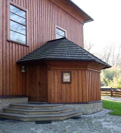 Zdjęcie nr 42: Kościół drewniany, orientowany, jednonawowy, wzniesiony na niewielkiej ceglanej podmurówce, o konstrukcji zrębowej, ściany szalowane pionowo z listowaniem, kruchta zachodnia o konstrukcji słupowo-ramowej. Nawa na rzucie prostokąta zbliżonego do kwadratu, prezbiterium węższe od nawy, wydłużone, zamknięte trójbocznie. Do północnej ściany prezbiterium przylega zakrystia na planie prostokąta. Do północnej ściany nawy przywiera niewielka kruchta na planie prostokąta, zamknięta trójbocznie. Przy zachodniej ścianie nawy znajduje się kruchta na rzucie prostokąta. Wnętrze nakryte pozornymi, spłaszczonymi sklepieniami o krzywiźnie przybierającej kształt łuku odcinkowego. Pomiędzy nawą a prezbiterium otwór tęczowy o wykroju prostokąta zbliżonego do kwadratu zamkniętego łukiem koszowym. Prezbiterium niższe od nawy, sięgające wysokości łuku tęczowego. Ściany prezbiterium i nawy obiega profilowany gzyms, oddzielający je od sklepień. W części zachodniej nawy parapet chóru muzycznego wsparty na dwóch kolumnach o stylizowanych kapitelach kompozytowych i kanelowanych trzonach na wysokich cokołach. W północno-zachodnim narożu drabiniaste schody prowadzące na chór w ośmiobocznej obudowie. Ściany i sklepienia pokryte polichromią. Na ścianach wzdłużnych oraz na osi ściany zachodniej otwory drzwiowe o prostokątnym wykroju zamknięte drzwiami spągowymi z desek oraz płycinowymi, na północnej ścianie prezbiterium prostokątny otwór drzwiowy do zakrystii. Posadzka z płyt kamiennych, szachownicowa. Kruchty i zakrystia nakryte stropami, przez nie dostęp do wnętrza. 
Elewacja frontowa jednoosiowa, zamknięta trójkątnym szczytem, poprzedzona kruchtą. Na osi wejście do kruchty zachodniej w postaci dwuskrzydłowych drzwi w formie stojącego prostokąta. Nad kruchtą pięterko dzwonowe z prostokątnym otworem zamykanym dwuskrzydłowymi okiennicami. Elewacja boczna południowa z czterema oknami, po dwa w nawie i prezbiterium. Elewacja północna przepruta dwoma oknami w części nawy. Okna krosnowe, w formie stojącego prostokąta, o niewielkich podziałach kwaterowych z witrażami. Na wschodniej ścianie kruchty północnej okno i jednoskrzydłowe drzwi. W zakrystii okno na ścianie północnej i drzwi jednoskrzydłowe na ścianie wschodniej. Kościół nakrywają dachy dwuspadowe, wyższy nad korpusem nawowym, niższy nad prezbiterium. Kruchta zachodnia w formie przysadzistej wieży, niższej od korpusu nawowego z pięterkiem dzwonowym, zwieńczonym hełmem baniastym, pokrytym gontem z iglicą oraz gałką i krzyżem. Kruchta północna z dachem wielospadowym. Zakrystia nakryta dachem pulpitowym. W połowie wysokości dachu znajduje się wieżyczka na sygnaturkę na ośmiobocznym obitym blachą trzonie, z ażurową latarnią nakrytą baniastym hełmem zakończonym kulą z krzyżem. 



