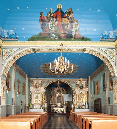 Zdjęcie nr 23: Kościół drewniany, orientowany, z dwuczęściowym korpusem: od wschodu jednonawowym, od zachodu trójnawowym; z prezbiterium zamkniętym trójbocznie, przy którym zakrystia od północy, z przybudówką od południa i dwiema wieżami od zachodu. Od wschodu chór muzyczny wbudowany pomiędzy wieże. Kościół wzniesiono w konstrukcji zrębowej, wieże w słupowo-ramowej, ściany oszalowane pionowym listwowaniem. 
Ściany prezbiterium i wschodniej części korpusu podzielone pseudokolumnami, zachodnia część podzielona kolumnami dźwigającymi architraw. Prezbiterium oddziela półokrągły łuk tęczowy; wschodnią i zachodnią część nawy łuk spłaszczony. Wschodnią część nawy oraz nawy boczne części zachodniej przekrywa płaski strop, zachodnią pozorne sklepienie zwierciadlane. Ściany oraz stropy pokryte polichromią figuralną, ornamentalną oraz roślinną: w prezbiterium namalowano wizerunek Ukrzyżowanego Chrystusa, przed łukiem tęczowym Matkę Boską w otoczeniu tajemnic różańcowych. Strop nawy imituje gwiaździste niebo. Posadzka kamienna. Wejście główne od zachodu, dwoje drzwi spod wież, kolejne od południa, przez przedsionek (babiniec), do zakrystii prowadzi portal zamknięty łukiem nadwieszonym. Cztery okna w prezbiterium o wykroju prostokątnym zamkniętym łukiem nadwieszonym, cztery we wschodniej części nawy o takim samym kształcie, cztery w zachodniej części zamknięte podwójnym łukiem kotarowym, dwa w zakrystii, południowej przybudówce, po dwa wysokie, wąskie okna w wieżach. Fasada dwuwieżowa, trójosiowa, trójkondygnacyjna. Przed wejściem kruchta zwieńczona dachem dwuspadowym, do której prowadzą dwuskrzydłowe drzwi w kształcie prostokątów, ściany boczne przeprute oknami. Powyżej dwie gładkie kondygnacje przedzielone dachem pulpitowym. Wieże trójkondygnacyjne, w dolnej kondygnacji drzwi, w wyższej okna w kształcie stojących prostokątów zamkniętych łukiem ostrym z wyciętym od dołu fragmentem pięcioliścia, powyżej ażurowa koronka. Ostatnią kondygnację tworzy izbica z nadwieszonym gankiem zamkniętym łukami spłaszczonymi. Od zewnątrz wyraźny podział na bryły, ściany gładkie. Każdą część przykrywa gontowy dach dwuspadowy, wspólny dla prezbiterium i starszej części, osobny dla nowszej części nawy; wieże nakryte hełmami namiotowymi, na kalenicy nawy baniasta wieżyczka na sygnaturkę z latarnią.  
