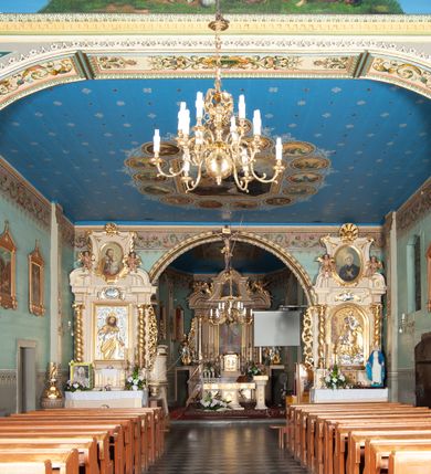 Zdjęcie nr 3: Kościół drewniany, orientowany, z dwuczęściowym korpusem: od wschodu jednonawowym, od zachodu trójnawowym; z prezbiterium zamkniętym trójbocznie, przy którym zakrystia od północy, z przybudówką od południa i dwiema wieżami od zachodu. Od wschodu chór muzyczny wbudowany pomiędzy wieże. Kościół wzniesiono w konstrukcji zrębowej, wieże w słupowo-ramowej, ściany oszalowane pionowym listwowaniem. 
Ściany prezbiterium i wschodniej części korpusu podzielone pseudokolumnami, zachodnia część podzielona kolumnami dźwigającymi architraw. Prezbiterium oddziela półokrągły łuk tęczowy; wschodnią i zachodnią część nawy łuk spłaszczony. Wschodnią część nawy oraz nawy boczne części zachodniej przekrywa płaski strop, zachodnią pozorne sklepienie zwierciadlane. Ściany oraz stropy pokryte polichromią figuralną, ornamentalną oraz roślinną: w prezbiterium namalowano wizerunek Ukrzyżowanego Chrystusa, przed łukiem tęczowym Matkę Boską w otoczeniu tajemnic różańcowych. Strop nawy imituje gwiaździste niebo. Posadzka kamienna. Wejście główne od zachodu, dwoje drzwi spod wież, kolejne od południa, przez przedsionek (babiniec), do zakrystii prowadzi portal zamknięty łukiem nadwieszonym. Cztery okna w prezbiterium o wykroju prostokątnym zamkniętym łukiem nadwieszonym, cztery we wschodniej części nawy o takim samym kształcie, cztery w zachodniej części zamknięte podwójnym łukiem kotarowym, dwa w zakrystii, południowej przybudówce, po dwa wysokie, wąskie okna w wieżach. Fasada dwuwieżowa, trójosiowa, trójkondygnacyjna. Przed wejściem kruchta zwieńczona dachem dwuspadowym, do której prowadzą dwuskrzydłowe drzwi w kształcie prostokątów, ściany boczne przeprute oknami. Powyżej dwie gładkie kondygnacje przedzielone dachem pulpitowym. Wieże trójkondygnacyjne, w dolnej kondygnacji drzwi, w wyższej okna w kształcie stojących prostokątów zamkniętych łukiem ostrym z wyciętym od dołu fragmentem pięcioliścia, powyżej ażurowa koronka. Ostatnią kondygnację tworzy izbica z nadwieszonym gankiem zamkniętym łukami spłaszczonymi. Od zewnątrz wyraźny podział na bryły, ściany gładkie. Każdą część przykrywa gontowy dach dwuspadowy, wspólny dla prezbiterium i starszej części, osobny dla nowszej części nawy; wieże nakryte hełmami namiotowymi, na kalenicy nawy baniasta wieżyczka na sygnaturkę z latarnią.  