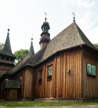 Zdjęcie nr 18: Kościół drewniany, orientowany, z dwuczęściowym korpusem: od wschodu jednonawowym, od zachodu trójnawowym; z prezbiterium zamkniętym trójbocznie, przy którym zakrystia od północy, z przybudówką od południa i dwiema wieżami od zachodu. Od wschodu chór muzyczny wbudowany pomiędzy wieże. Kościół wzniesiono w konstrukcji zrębowej, wieże w słupowo-ramowej, ściany oszalowane pionowym listwowaniem. 
Ściany prezbiterium i wschodniej części korpusu podzielone pseudokolumnami, zachodnia część podzielona kolumnami dźwigającymi architraw. Prezbiterium oddziela półokrągły łuk tęczowy; wschodnią i zachodnią część nawy łuk spłaszczony. Wschodnią część nawy oraz nawy boczne części zachodniej przekrywa płaski strop, zachodnią pozorne sklepienie zwierciadlane. Ściany oraz stropy pokryte polichromią figuralną, ornamentalną oraz roślinną: w prezbiterium namalowano wizerunek Ukrzyżowanego Chrystusa, przed łukiem tęczowym Matkę Boską w otoczeniu tajemnic różańcowych. Strop nawy imituje gwiaździste niebo. Posadzka kamienna. Wejście główne od zachodu, dwoje drzwi spod wież, kolejne od południa, przez przedsionek (babiniec), do zakrystii prowadzi portal zamknięty łukiem nadwieszonym. Cztery okna w prezbiterium o wykroju prostokątnym zamkniętym łukiem nadwieszonym, cztery we wschodniej części nawy o takim samym kształcie, cztery w zachodniej części zamknięte podwójnym łukiem kotarowym, dwa w zakrystii, południowej przybudówce, po dwa wysokie, wąskie okna w wieżach. Fasada dwuwieżowa, trójosiowa, trójkondygnacyjna. Przed wejściem kruchta zwieńczona dachem dwuspadowym, do której prowadzą dwuskrzydłowe drzwi w kształcie prostokątów, ściany boczne przeprute oknami. Powyżej dwie gładkie kondygnacje przedzielone dachem pulpitowym. Wieże trójkondygnacyjne, w dolnej kondygnacji drzwi, w wyższej okna w kształcie stojących prostokątów zamkniętych łukiem ostrym z wyciętym od dołu fragmentem pięcioliścia, powyżej ażurowa koronka. Ostatnią kondygnację tworzy izbica z nadwieszonym gankiem zamkniętym łukami spłaszczonymi. Od zewnątrz wyraźny podział na bryły, ściany gładkie. Każdą część przykrywa gontowy dach dwuspadowy, wspólny dla prezbiterium i starszej części, osobny dla nowszej części nawy; wieże nakryte hełmami namiotowymi, na kalenicy nawy baniasta wieżyczka na sygnaturkę z latarnią.  