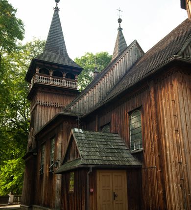 Zdjęcie nr 19: Kościół drewniany, orientowany, z dwuczęściowym korpusem: od wschodu jednonawowym, od zachodu trójnawowym; z prezbiterium zamkniętym trójbocznie, przy którym zakrystia od północy, z przybudówką od południa i dwiema wieżami od zachodu. Od wschodu chór muzyczny wbudowany pomiędzy wieże. Kościół wzniesiono w konstrukcji zrębowej, wieże w słupowo-ramowej, ściany oszalowane pionowym listwowaniem. 
Ściany prezbiterium i wschodniej części korpusu podzielone pseudokolumnami, zachodnia część podzielona kolumnami dźwigającymi architraw. Prezbiterium oddziela półokrągły łuk tęczowy; wschodnią i zachodnią część nawy łuk spłaszczony. Wschodnią część nawy oraz nawy boczne części zachodniej przekrywa płaski strop, zachodnią pozorne sklepienie zwierciadlane. Ściany oraz stropy pokryte polichromią figuralną, ornamentalną oraz roślinną: w prezbiterium namalowano wizerunek Ukrzyżowanego Chrystusa, przed łukiem tęczowym Matkę Boską w otoczeniu tajemnic różańcowych. Strop nawy imituje gwiaździste niebo. Posadzka kamienna. Wejście główne od zachodu, dwoje drzwi spod wież, kolejne od południa, przez przedsionek (babiniec), do zakrystii prowadzi portal zamknięty łukiem nadwieszonym. Cztery okna w prezbiterium o wykroju prostokątnym zamkniętym łukiem nadwieszonym, cztery we wschodniej części nawy o takim samym kształcie, cztery w zachodniej części zamknięte podwójnym łukiem kotarowym, dwa w zakrystii, południowej przybudówce, po dwa wysokie, wąskie okna w wieżach. Fasada dwuwieżowa, trójosiowa, trójkondygnacyjna. Przed wejściem kruchta zwieńczona dachem dwuspadowym, do której prowadzą dwuskrzydłowe drzwi w kształcie prostokątów, ściany boczne przeprute oknami. Powyżej dwie gładkie kondygnacje przedzielone dachem pulpitowym. Wieże trójkondygnacyjne, w dolnej kondygnacji drzwi, w wyższej okna w kształcie stojących prostokątów zamkniętych łukiem ostrym z wyciętym od dołu fragmentem pięcioliścia, powyżej ażurowa koronka. Ostatnią kondygnację tworzy izbica z nadwieszonym gankiem zamkniętym łukami spłaszczonymi. Od zewnątrz wyraźny podział na bryły, ściany gładkie. Każdą część przykrywa gontowy dach dwuspadowy, wspólny dla prezbiterium i starszej części, osobny dla nowszej części nawy; wieże nakryte hełmami namiotowymi, na kalenicy nawy baniasta wieżyczka na sygnaturkę z latarnią.  