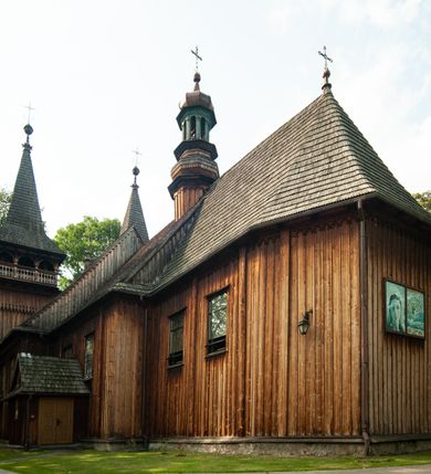 Zdjęcie nr 13: Kościół drewniany, orientowany, z dwuczęściowym korpusem: od wschodu jednonawowym, od zachodu trójnawowym; z prezbiterium zamkniętym trójbocznie, przy którym zakrystia od północy, z przybudówką od południa i dwiema wieżami od zachodu. Od wschodu chór muzyczny wbudowany pomiędzy wieże. Kościół wzniesiono w konstrukcji zrębowej, wieże w słupowo-ramowej, ściany oszalowane pionowym listwowaniem. 
Ściany prezbiterium i wschodniej części korpusu podzielone pseudokolumnami, zachodnia część podzielona kolumnami dźwigającymi architraw. Prezbiterium oddziela półokrągły łuk tęczowy; wschodnią i zachodnią część nawy łuk spłaszczony. Wschodnią część nawy oraz nawy boczne części zachodniej przekrywa płaski strop, zachodnią pozorne sklepienie zwierciadlane. Ściany oraz stropy pokryte polichromią figuralną, ornamentalną oraz roślinną: w prezbiterium namalowano wizerunek Ukrzyżowanego Chrystusa, przed łukiem tęczowym Matkę Boską w otoczeniu tajemnic różańcowych. Strop nawy imituje gwiaździste niebo. Posadzka kamienna. Wejście główne od zachodu, dwoje drzwi spod wież, kolejne od południa, przez przedsionek (babiniec), do zakrystii prowadzi portal zamknięty łukiem nadwieszonym. Cztery okna w prezbiterium o wykroju prostokątnym zamkniętym łukiem nadwieszonym, cztery we wschodniej części nawy o takim samym kształcie, cztery w zachodniej części zamknięte podwójnym łukiem kotarowym, dwa w zakrystii, południowej przybudówce, po dwa wysokie, wąskie okna w wieżach. Fasada dwuwieżowa, trójosiowa, trójkondygnacyjna. Przed wejściem kruchta zwieńczona dachem dwuspadowym, do której prowadzą dwuskrzydłowe drzwi w kształcie prostokątów, ściany boczne przeprute oknami. Powyżej dwie gładkie kondygnacje przedzielone dachem pulpitowym. Wieże trójkondygnacyjne, w dolnej kondygnacji drzwi, w wyższej okna w kształcie stojących prostokątów zamkniętych łukiem ostrym z wyciętym od dołu fragmentem pięcioliścia, powyżej ażurowa koronka. Ostatnią kondygnację tworzy izbica z nadwieszonym gankiem zamkniętym łukami spłaszczonymi. Od zewnątrz wyraźny podział na bryły, ściany gładkie. Każdą część przykrywa gontowy dach dwuspadowy, wspólny dla prezbiterium i starszej części, osobny dla nowszej części nawy; wieże nakryte hełmami namiotowymi, na kalenicy nawy baniasta wieżyczka na sygnaturkę z latarnią.  