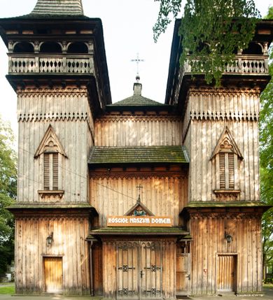 Zdjęcie nr 1: Kościół drewniany, orientowany, z dwuczęściowym korpusem: od wschodu jednonawowym, od zachodu trójnawowym; z prezbiterium zamkniętym trójbocznie, przy którym zakrystia od północy, z przybudówką od południa i dwiema wieżami od zachodu. Od wschodu chór muzyczny wbudowany pomiędzy wieże. Kościół wzniesiono w konstrukcji zrębowej, wieże w słupowo-ramowej, ściany oszalowane pionowym listwowaniem. 
Ściany prezbiterium i wschodniej części korpusu podzielone pseudokolumnami, zachodnia część podzielona kolumnami dźwigającymi architraw. Prezbiterium oddziela półokrągły łuk tęczowy; wschodnią i zachodnią część nawy łuk spłaszczony. Wschodnią część nawy oraz nawy boczne części zachodniej przekrywa płaski strop, zachodnią pozorne sklepienie zwierciadlane. Ściany oraz stropy pokryte polichromią figuralną, ornamentalną oraz roślinną: w prezbiterium namalowano wizerunek Ukrzyżowanego Chrystusa, przed łukiem tęczowym Matkę Boską w otoczeniu tajemnic różańcowych. Strop nawy imituje gwiaździste niebo. Posadzka kamienna. Wejście główne od zachodu, dwoje drzwi spod wież, kolejne od południa, przez przedsionek (babiniec), do zakrystii prowadzi portal zamknięty łukiem nadwieszonym. Cztery okna w prezbiterium o wykroju prostokątnym zamkniętym łukiem nadwieszonym, cztery we wschodniej części nawy o takim samym kształcie, cztery w zachodniej części zamknięte podwójnym łukiem kotarowym, dwa w zakrystii, południowej przybudówce, po dwa wysokie, wąskie okna w wieżach. Fasada dwuwieżowa, trójosiowa, trójkondygnacyjna. Przed wejściem kruchta zwieńczona dachem dwuspadowym, do której prowadzą dwuskrzydłowe drzwi w kształcie prostokątów, ściany boczne przeprute oknami. Powyżej dwie gładkie kondygnacje przedzielone dachem pulpitowym. Wieże trójkondygnacyjne, w dolnej kondygnacji drzwi, w wyższej okna w kształcie stojących prostokątów zamkniętych łukiem ostrym z wyciętym od dołu fragmentem pięcioliścia, powyżej ażurowa koronka. Ostatnią kondygnację tworzy izbica z nadwieszonym gankiem zamkniętym łukami spłaszczonymi. Od zewnątrz wyraźny podział na bryły, ściany gładkie. Każdą część przykrywa gontowy dach dwuspadowy, wspólny dla prezbiterium i starszej części, osobny dla nowszej części nawy; wieże nakryte hełmami namiotowymi, na kalenicy nawy baniasta wieżyczka na sygnaturkę z latarnią.  