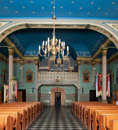 Zdjęcie nr 11: Kościół drewniany, orientowany, z dwuczęściowym korpusem: od wschodu jednonawowym, od zachodu trójnawowym; z prezbiterium zamkniętym trójbocznie, przy którym zakrystia od północy, z przybudówką od południa i dwiema wieżami od zachodu. Od wschodu chór muzyczny wbudowany pomiędzy wieże. Kościół wzniesiono w konstrukcji zrębowej, wieże w słupowo-ramowej, ściany oszalowane pionowym listwowaniem. 
Ściany prezbiterium i wschodniej części korpusu podzielone pseudokolumnami, zachodnia część podzielona kolumnami dźwigającymi architraw. Prezbiterium oddziela półokrągły łuk tęczowy; wschodnią i zachodnią część nawy łuk spłaszczony. Wschodnią część nawy oraz nawy boczne części zachodniej przekrywa płaski strop, zachodnią pozorne sklepienie zwierciadlane. Ściany oraz stropy pokryte polichromią figuralną, ornamentalną oraz roślinną: w prezbiterium namalowano wizerunek Ukrzyżowanego Chrystusa, przed łukiem tęczowym Matkę Boską w otoczeniu tajemnic różańcowych. Strop nawy imituje gwiaździste niebo. Posadzka kamienna. Wejście główne od zachodu, dwoje drzwi spod wież, kolejne od południa, przez przedsionek (babiniec), do zakrystii prowadzi portal zamknięty łukiem nadwieszonym. Cztery okna w prezbiterium o wykroju prostokątnym zamkniętym łukiem nadwieszonym, cztery we wschodniej części nawy o takim samym kształcie, cztery w zachodniej części zamknięte podwójnym łukiem kotarowym, dwa w zakrystii, południowej przybudówce, po dwa wysokie, wąskie okna w wieżach. Fasada dwuwieżowa, trójosiowa, trójkondygnacyjna. Przed wejściem kruchta zwieńczona dachem dwuspadowym, do której prowadzą dwuskrzydłowe drzwi w kształcie prostokątów, ściany boczne przeprute oknami. Powyżej dwie gładkie kondygnacje przedzielone dachem pulpitowym. Wieże trójkondygnacyjne, w dolnej kondygnacji drzwi, w wyższej okna w kształcie stojących prostokątów zamkniętych łukiem ostrym z wyciętym od dołu fragmentem pięcioliścia, powyżej ażurowa koronka. Ostatnią kondygnację tworzy izbica z nadwieszonym gankiem zamkniętym łukami spłaszczonymi. Od zewnątrz wyraźny podział na bryły, ściany gładkie. Każdą część przykrywa gontowy dach dwuspadowy, wspólny dla prezbiterium i starszej części, osobny dla nowszej części nawy; wieże nakryte hełmami namiotowymi, na kalenicy nawy baniasta wieżyczka na sygnaturkę z latarnią.  