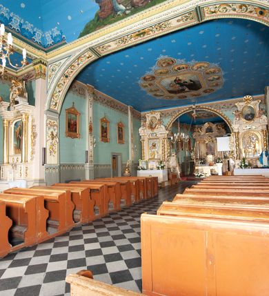 Zdjęcie nr 7: Kościół drewniany, orientowany, z dwuczęściowym korpusem: od wschodu jednonawowym, od zachodu trójnawowym; z prezbiterium zamkniętym trójbocznie, przy którym zakrystia od północy, z przybudówką od południa i dwiema wieżami od zachodu. Od wschodu chór muzyczny wbudowany pomiędzy wieże. Kościół wzniesiono w konstrukcji zrębowej, wieże w słupowo-ramowej, ściany oszalowane pionowym listwowaniem. 
Ściany prezbiterium i wschodniej części korpusu podzielone pseudokolumnami, zachodnia część podzielona kolumnami dźwigającymi architraw. Prezbiterium oddziela półokrągły łuk tęczowy; wschodnią i zachodnią część nawy łuk spłaszczony. Wschodnią część nawy oraz nawy boczne części zachodniej przekrywa płaski strop, zachodnią pozorne sklepienie zwierciadlane. Ściany oraz stropy pokryte polichromią figuralną, ornamentalną oraz roślinną: w prezbiterium namalowano wizerunek Ukrzyżowanego Chrystusa, przed łukiem tęczowym Matkę Boską w otoczeniu tajemnic różańcowych. Strop nawy imituje gwiaździste niebo. Posadzka kamienna. Wejście główne od zachodu, dwoje drzwi spod wież, kolejne od południa, przez przedsionek (babiniec), do zakrystii prowadzi portal zamknięty łukiem nadwieszonym. Cztery okna w prezbiterium o wykroju prostokątnym zamkniętym łukiem nadwieszonym, cztery we wschodniej części nawy o takim samym kształcie, cztery w zachodniej części zamknięte podwójnym łukiem kotarowym, dwa w zakrystii, południowej przybudówce, po dwa wysokie, wąskie okna w wieżach. Fasada dwuwieżowa, trójosiowa, trójkondygnacyjna. Przed wejściem kruchta zwieńczona dachem dwuspadowym, do której prowadzą dwuskrzydłowe drzwi w kształcie prostokątów, ściany boczne przeprute oknami. Powyżej dwie gładkie kondygnacje przedzielone dachem pulpitowym. Wieże trójkondygnacyjne, w dolnej kondygnacji drzwi, w wyższej okna w kształcie stojących prostokątów zamkniętych łukiem ostrym z wyciętym od dołu fragmentem pięcioliścia, powyżej ażurowa koronka. Ostatnią kondygnację tworzy izbica z nadwieszonym gankiem zamkniętym łukami spłaszczonymi. Od zewnątrz wyraźny podział na bryły, ściany gładkie. Każdą część przykrywa gontowy dach dwuspadowy, wspólny dla prezbiterium i starszej części, osobny dla nowszej części nawy; wieże nakryte hełmami namiotowymi, na kalenicy nawy baniasta wieżyczka na sygnaturkę z latarnią.  