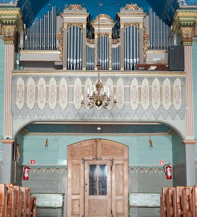 Zdjęcie nr 14: Kościół drewniany, orientowany, z dwuczęściowym korpusem: od wschodu jednonawowym, od zachodu trójnawowym; z prezbiterium zamkniętym trójbocznie, przy którym zakrystia od północy, z przybudówką od południa i dwiema wieżami od zachodu. Od wschodu chór muzyczny wbudowany pomiędzy wieże. Kościół wzniesiono w konstrukcji zrębowej, wieże w słupowo-ramowej, ściany oszalowane pionowym listwowaniem. 
Ściany prezbiterium i wschodniej części korpusu podzielone pseudokolumnami, zachodnia część podzielona kolumnami dźwigającymi architraw. Prezbiterium oddziela półokrągły łuk tęczowy; wschodnią i zachodnią część nawy łuk spłaszczony. Wschodnią część nawy oraz nawy boczne części zachodniej przekrywa płaski strop, zachodnią pozorne sklepienie zwierciadlane. Ściany oraz stropy pokryte polichromią figuralną, ornamentalną oraz roślinną: w prezbiterium namalowano wizerunek Ukrzyżowanego Chrystusa, przed łukiem tęczowym Matkę Boską w otoczeniu tajemnic różańcowych. Strop nawy imituje gwiaździste niebo. Posadzka kamienna. Wejście główne od zachodu, dwoje drzwi spod wież, kolejne od południa, przez przedsionek (babiniec), do zakrystii prowadzi portal zamknięty łukiem nadwieszonym. Cztery okna w prezbiterium o wykroju prostokątnym zamkniętym łukiem nadwieszonym, cztery we wschodniej części nawy o takim samym kształcie, cztery w zachodniej części zamknięte podwójnym łukiem kotarowym, dwa w zakrystii, południowej przybudówce, po dwa wysokie, wąskie okna w wieżach. Fasada dwuwieżowa, trójosiowa, trójkondygnacyjna. Przed wejściem kruchta zwieńczona dachem dwuspadowym, do której prowadzą dwuskrzydłowe drzwi w kształcie prostokątów, ściany boczne przeprute oknami. Powyżej dwie gładkie kondygnacje przedzielone dachem pulpitowym. Wieże trójkondygnacyjne, w dolnej kondygnacji drzwi, w wyższej okna w kształcie stojących prostokątów zamkniętych łukiem ostrym z wyciętym od dołu fragmentem pięcioliścia, powyżej ażurowa koronka. Ostatnią kondygnację tworzy izbica z nadwieszonym gankiem zamkniętym łukami spłaszczonymi. Od zewnątrz wyraźny podział na bryły, ściany gładkie. Każdą część przykrywa gontowy dach dwuspadowy, wspólny dla prezbiterium i starszej części, osobny dla nowszej części nawy; wieże nakryte hełmami namiotowymi, na kalenicy nawy baniasta wieżyczka na sygnaturkę z latarnią.  