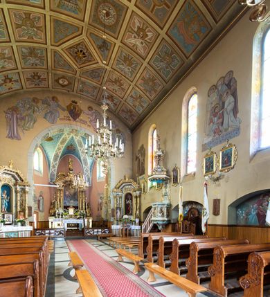 Zdjęcie nr 16: Kościół jest budowlą orientowaną, założoną na planie wydłużonego prostokąta, murowaną, jednonawową z prezbiterium i zakrystią (od północy). Prezbiterium jest węższe od nawy, zamknięte wielobocznie, oddziela je tęcza o łuku półkolistym. Od zachodu chór zamknięty balustradą załamaną trójbocznie i wysuniętą przed lico w części środkowej, dekorowaną płycinami z wicią roślinną. Ściany wnętrza gładkie, brak podziałów pionowych, poziomy podział tworzą przy ziemi nisze zamknięte łukiem odcinkowym; dół ścian wyłożony drewnianą boazerią. Ściany przeprute oknami – prezbiterium dwoma, nawa ośmioma w kształcie stojącego prostokąta zamkniętego łukiem półkolistym; większość wypełniają witraże. Cztery okna w zakrystii. Główne wejście przez korpus wieżowy od zachodu, drugie od zakrystii. Elewacje kościoła są gładkie, górne partie z cegieł, dolne oraz naroża podkreślone okładziną kamienną. Wokół, poniżej partii okien kapnik. Wieża z wejściem umieszczonym w glifie w kształcie stojącego prostokąta zamkniętego łukiem odcinkowym, chronionym daszkiem, ponad którym niewielkie okno. W górnej partii z każdej strony małe okno, pod dachem arkady zamknięte półkoliście, po trzy na każdą stronę. Środkowa arkada ściany frontowej przysłonięta tarczą zegara. Dach nawy dwuspadowy, prezbiterium i zakrystii wieloboczny, ponad nawą kamienna wieżyczka na sygnaturkę, wieża przekryta hełmem namiotowym. Od zewnątrz, na wschodniej ścianie prezbiterium figura ukrzyżowanego Jezusa. Najcenniejszym zabytkiem kościoła jest siedemnastowieczny ołtarz główny, który w poprzedniej budowli stanowił ołtarz boczny. Polichromię zaprojektowała Jadwiga Rymar z Krakowa.