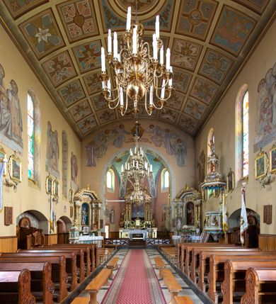 Zdjęcie nr 12: Kościół jest budowlą orientowaną, założoną na planie wydłużonego prostokąta, murowaną, jednonawową z prezbiterium i zakrystią (od północy). Prezbiterium jest węższe od nawy, zamknięte wielobocznie, oddziela je tęcza o łuku półkolistym. Od zachodu chór zamknięty balustradą załamaną trójbocznie i wysuniętą przed lico w części środkowej, dekorowaną płycinami z wicią roślinną. Ściany wnętrza gładkie, brak podziałów pionowych, poziomy podział tworzą przy ziemi nisze zamknięte łukiem odcinkowym; dół ścian wyłożony drewnianą boazerią. Ściany przeprute oknami – prezbiterium dwoma, nawa ośmioma w kształcie stojącego prostokąta zamkniętego łukiem półkolistym; większość wypełniają witraże. Cztery okna w zakrystii. Główne wejście przez korpus wieżowy od zachodu, drugie od zakrystii. Elewacje kościoła są gładkie, górne partie z cegieł, dolne oraz naroża podkreślone okładziną kamienną. Wokół, poniżej partii okien kapnik. Wieża z wejściem umieszczonym w glifie w kształcie stojącego prostokąta zamkniętego łukiem odcinkowym, chronionym daszkiem, ponad którym niewielkie okno. W górnej partii z każdej strony małe okno, pod dachem arkady zamknięte półkoliście, po trzy na każdą stronę. Środkowa arkada ściany frontowej przysłonięta tarczą zegara. Dach nawy dwuspadowy, prezbiterium i zakrystii wieloboczny, ponad nawą kamienna wieżyczka na sygnaturkę, wieża przekryta hełmem namiotowym. Od zewnątrz, na wschodniej ścianie prezbiterium figura ukrzyżowanego Jezusa. Najcenniejszym zabytkiem kościoła jest siedemnastowieczny ołtarz główny, który w poprzedniej budowli stanowił ołtarz boczny. Polichromię zaprojektowała Jadwiga Rymar z Krakowa.