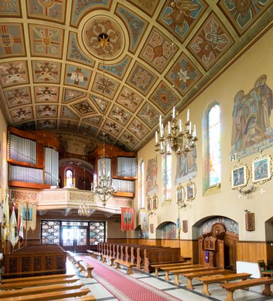 Zdjęcie nr 17: Kościół jest budowlą orientowaną, założoną na planie wydłużonego prostokąta, murowaną, jednonawową z prezbiterium i zakrystią (od północy). Prezbiterium jest węższe od nawy, zamknięte wielobocznie, oddziela je tęcza o łuku półkolistym. Od zachodu chór zamknięty balustradą załamaną trójbocznie i wysuniętą przed lico w części środkowej, dekorowaną płycinami z wicią roślinną. Ściany wnętrza gładkie, brak podziałów pionowych, poziomy podział tworzą przy ziemi nisze zamknięte łukiem odcinkowym; dół ścian wyłożony drewnianą boazerią. Ściany przeprute oknami – prezbiterium dwoma, nawa ośmioma w kształcie stojącego prostokąta zamkniętego łukiem półkolistym; większość wypełniają witraże. Cztery okna w zakrystii. Główne wejście przez korpus wieżowy od zachodu, drugie od zakrystii. Elewacje kościoła są gładkie, górne partie z cegieł, dolne oraz naroża podkreślone okładziną kamienną. Wokół, poniżej partii okien kapnik. Wieża z wejściem umieszczonym w glifie w kształcie stojącego prostokąta zamkniętego łukiem odcinkowym, chronionym daszkiem, ponad którym niewielkie okno. W górnej partii z każdej strony małe okno, pod dachem arkady zamknięte półkoliście, po trzy na każdą stronę. Środkowa arkada ściany frontowej przysłonięta tarczą zegara. Dach nawy dwuspadowy, prezbiterium i zakrystii wieloboczny, ponad nawą kamienna wieżyczka na sygnaturkę, wieża przekryta hełmem namiotowym. Od zewnątrz, na wschodniej ścianie prezbiterium figura ukrzyżowanego Jezusa. Najcenniejszym zabytkiem kościoła jest siedemnastowieczny ołtarz główny, który w poprzedniej budowli stanowił ołtarz boczny. Polichromię zaprojektowała Jadwiga Rymar z Krakowa.