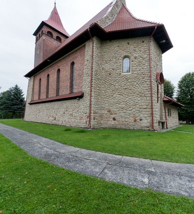 Zdjęcie nr 7: Kościół jest budowlą orientowaną, założoną na planie wydłużonego prostokąta, murowaną, jednonawową z prezbiterium i zakrystią (od północy). Prezbiterium jest węższe od nawy, zamknięte wielobocznie, oddziela je tęcza o łuku półkolistym. Od zachodu chór zamknięty balustradą załamaną trójbocznie i wysuniętą przed lico w części środkowej, dekorowaną płycinami z wicią roślinną. Ściany wnętrza gładkie, brak podziałów pionowych, poziomy podział tworzą przy ziemi nisze zamknięte łukiem odcinkowym; dół ścian wyłożony drewnianą boazerią. Ściany przeprute oknami – prezbiterium dwoma, nawa ośmioma w kształcie stojącego prostokąta zamkniętego łukiem półkolistym; większość wypełniają witraże. Cztery okna w zakrystii. Główne wejście przez korpus wieżowy od zachodu, drugie od zakrystii. Elewacje kościoła są gładkie, górne partie z cegieł, dolne oraz naroża podkreślone okładziną kamienną. Wokół, poniżej partii okien kapnik. Wieża z wejściem umieszczonym w glifie w kształcie stojącego prostokąta zamkniętego łukiem odcinkowym, chronionym daszkiem, ponad którym niewielkie okno. W górnej partii z każdej strony małe okno, pod dachem arkady zamknięte półkoliście, po trzy na każdą stronę. Środkowa arkada ściany frontowej przysłonięta tarczą zegara. Dach nawy dwuspadowy, prezbiterium i zakrystii wieloboczny, ponad nawą kamienna wieżyczka na sygnaturkę, wieża przekryta hełmem namiotowym. Od zewnątrz, na wschodniej ścianie prezbiterium figura ukrzyżowanego Jezusa. Najcenniejszym zabytkiem kościoła jest siedemnastowieczny ołtarz główny, który w poprzedniej budowli stanowił ołtarz boczny. Polichromię zaprojektowała Jadwiga Rymar z Krakowa.