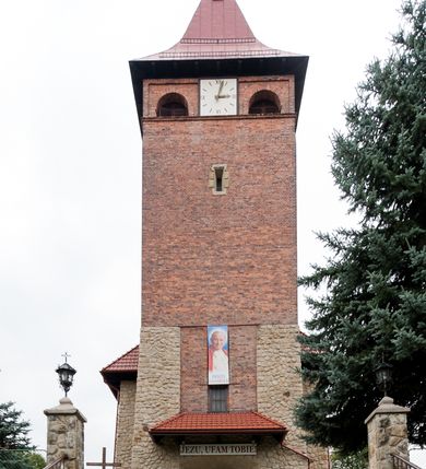 Zdjęcie nr 4: Kościół jest budowlą orientowaną, założoną na planie wydłużonego prostokąta, murowaną, jednonawową z prezbiterium i zakrystią (od północy). Prezbiterium jest węższe od nawy, zamknięte wielobocznie, oddziela je tęcza o łuku półkolistym. Od zachodu chór zamknięty balustradą załamaną trójbocznie i wysuniętą przed lico w części środkowej, dekorowaną płycinami z wicią roślinną. Ściany wnętrza gładkie, brak podziałów pionowych, poziomy podział tworzą przy ziemi nisze zamknięte łukiem odcinkowym; dół ścian wyłożony drewnianą boazerią. Ściany przeprute oknami – prezbiterium dwoma, nawa ośmioma w kształcie stojącego prostokąta zamkniętego łukiem półkolistym; większość wypełniają witraże. Cztery okna w zakrystii. Główne wejście przez korpus wieżowy od zachodu, drugie od zakrystii. Elewacje kościoła są gładkie, górne partie z cegieł, dolne oraz naroża podkreślone okładziną kamienną. Wokół, poniżej partii okien kapnik. Wieża z wejściem umieszczonym w glifie w kształcie stojącego prostokąta zamkniętego łukiem odcinkowym, chronionym daszkiem, ponad którym niewielkie okno. W górnej partii z każdej strony małe okno, pod dachem arkady zamknięte półkoliście, po trzy na każdą stronę. Środkowa arkada ściany frontowej przysłonięta tarczą zegara. Dach nawy dwuspadowy, prezbiterium i zakrystii wieloboczny, ponad nawą kamienna wieżyczka na sygnaturkę, wieża przekryta hełmem namiotowym. Od zewnątrz, na wschodniej ścianie prezbiterium figura ukrzyżowanego Jezusa. Najcenniejszym zabytkiem kościoła jest siedemnastowieczny ołtarz główny, który w poprzedniej budowli stanowił ołtarz boczny. Polichromię zaprojektowała Jadwiga Rymar z Krakowa.