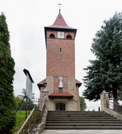 Zdjęcie nr 3: Kościół jest budowlą orientowaną, założoną na planie wydłużonego prostokąta, murowaną, jednonawową z prezbiterium i zakrystią (od północy). Prezbiterium jest węższe od nawy, zamknięte wielobocznie, oddziela je tęcza o łuku półkolistym. Od zachodu chór zamknięty balustradą załamaną trójbocznie i wysuniętą przed lico w części środkowej, dekorowaną płycinami z wicią roślinną. Ściany wnętrza gładkie, brak podziałów pionowych, poziomy podział tworzą przy ziemi nisze zamknięte łukiem odcinkowym; dół ścian wyłożony drewnianą boazerią. Ściany przeprute oknami – prezbiterium dwoma, nawa ośmioma w kształcie stojącego prostokąta zamkniętego łukiem półkolistym; większość wypełniają witraże. Cztery okna w zakrystii. Główne wejście przez korpus wieżowy od zachodu, drugie od zakrystii. Elewacje kościoła są gładkie, górne partie z cegieł, dolne oraz naroża podkreślone okładziną kamienną. Wokół, poniżej partii okien kapnik. Wieża z wejściem umieszczonym w glifie w kształcie stojącego prostokąta zamkniętego łukiem odcinkowym, chronionym daszkiem, ponad którym niewielkie okno. W górnej partii z każdej strony małe okno, pod dachem arkady zamknięte półkoliście, po trzy na każdą stronę. Środkowa arkada ściany frontowej przysłonięta tarczą zegara. Dach nawy dwuspadowy, prezbiterium i zakrystii wieloboczny, ponad nawą kamienna wieżyczka na sygnaturkę, wieża przekryta hełmem namiotowym. Od zewnątrz, na wschodniej ścianie prezbiterium figura ukrzyżowanego Jezusa. Najcenniejszym zabytkiem kościoła jest siedemnastowieczny ołtarz główny, który w poprzedniej budowli stanowił ołtarz boczny. Polichromię zaprojektowała Jadwiga Rymar z Krakowa.