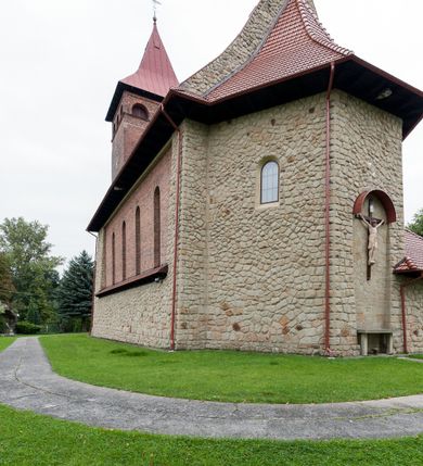 Zdjęcie nr 8: Kościół jest budowlą orientowaną, założoną na planie wydłużonego prostokąta, murowaną, jednonawową z prezbiterium i zakrystią (od północy). Prezbiterium jest węższe od nawy, zamknięte wielobocznie, oddziela je tęcza o łuku półkolistym. Od zachodu chór zamknięty balustradą załamaną trójbocznie i wysuniętą przed lico w części środkowej, dekorowaną płycinami z wicią roślinną. Ściany wnętrza gładkie, brak podziałów pionowych, poziomy podział tworzą przy ziemi nisze zamknięte łukiem odcinkowym; dół ścian wyłożony drewnianą boazerią. Ściany przeprute oknami – prezbiterium dwoma, nawa ośmioma w kształcie stojącego prostokąta zamkniętego łukiem półkolistym; większość wypełniają witraże. Cztery okna w zakrystii. Główne wejście przez korpus wieżowy od zachodu, drugie od zakrystii. Elewacje kościoła są gładkie, górne partie z cegieł, dolne oraz naroża podkreślone okładziną kamienną. Wokół, poniżej partii okien kapnik. Wieża z wejściem umieszczonym w glifie w kształcie stojącego prostokąta zamkniętego łukiem odcinkowym, chronionym daszkiem, ponad którym niewielkie okno. W górnej partii z każdej strony małe okno, pod dachem arkady zamknięte półkoliście, po trzy na każdą stronę. Środkowa arkada ściany frontowej przysłonięta tarczą zegara. Dach nawy dwuspadowy, prezbiterium i zakrystii wieloboczny, ponad nawą kamienna wieżyczka na sygnaturkę, wieża przekryta hełmem namiotowym. Od zewnątrz, na wschodniej ścianie prezbiterium figura ukrzyżowanego Jezusa. Najcenniejszym zabytkiem kościoła jest siedemnastowieczny ołtarz główny, który w poprzedniej budowli stanowił ołtarz boczny. Polichromię zaprojektowała Jadwiga Rymar z Krakowa.