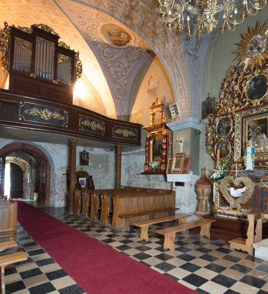 Zdjęcie nr 8: Kościół położony jest na wzniesieniu, obwiedziony dookoła niskim murem. Świątynia murowana, orientowana, jednonawowa na planie prostokątnej nawy z węższym prezbiterium zamkniętym półkoliście, z wieżą od zachodu; przykryty wysokim dwuspadowym dachem, z sygnaturką nad prezbiterium. Wieża czworoboczna, w przyziemiu mieszcząca kruchtę, wyżej przechodząca w ośmiobok, zwieńczona stylizowanym na gotycki, iglicowym, pokrytym blachą hełmem, flankowanym trójkątnymi szczycikami. Od południa kościoła usytuowana jest druga kruchta z kamiennym portalem, a od północy zakrystia z dodatkowym pomieszczeniem na paramenty liturgiczne, nad nimi empora. Prezbiterium oraz nawę obejmuje z zewnątrz sześć wysokich skarp. Wewnątrz podziały architektoniczne wydzielają przyścienne filary w nawie z silnie wysuniętym do wnętrza łukiem tęczy. Prezbiterium oraz nawę oświetla pięć wysokich okien, zamkniętych półkoliście, usytuowanych od południa. Portal główny wykonany z wapienia pińczowskiego o typie arkadowym z charakterystycznym układem kamiennych ciosów dźwiga boniowany łuk archiwolty. Nad nim trójkątny przyczółek, silnie wysunięty przed lico ściany, ujęty dookoła wydatnym, profilowanym gzymsem z kartuszem w polu z herbami: Lubicz, Leliwa, Junosza i Rawicz oraz inicjałami „ALDL” i datą „An[n]o D[omi]ni 1623”. Portal południowy z wapienia jurajskiego o wykroju zbliżonym do ostrołukowego (krzywo wycięty). Natomiast portal do zakrystii o renesansowej budowie i dekoracji. Nawa sklepiona krzyżowo-kolebkowo.
Do zewnętrznej, południowej ściany kościoła dostawiony jest pomnik nagrobny hrabiego Jakuba z Granowa i Eleonory z Dembowskich Wodzickich.