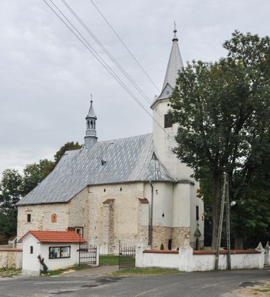 Zdjęcie nr 2: Kościół położony jest na wzniesieniu, obwiedziony dookoła niskim murem. Świątynia murowana, orientowana, jednonawowa na planie prostokątnej nawy z węższym prezbiterium zamkniętym półkoliście, z wieżą od zachodu; przykryty wysokim dwuspadowym dachem, z sygnaturką nad prezbiterium. Wieża czworoboczna, w przyziemiu mieszcząca kruchtę, wyżej przechodząca w ośmiobok, zwieńczona stylizowanym na gotycki, iglicowym, pokrytym blachą hełmem, flankowanym trójkątnymi szczycikami. Od południa kościoła usytuowana jest druga kruchta z kamiennym portalem, a od północy zakrystia z dodatkowym pomieszczeniem na paramenty liturgiczne, nad nimi empora. Prezbiterium oraz nawę obejmuje z zewnątrz sześć wysokich skarp. Wewnątrz podziały architektoniczne wydzielają przyścienne filary w nawie z silnie wysuniętym do wnętrza łukiem tęczy. Prezbiterium oraz nawę oświetla pięć wysokich okien, zamkniętych półkoliście, usytuowanych od południa. Portal główny wykonany z wapienia pińczowskiego o typie arkadowym z charakterystycznym układem kamiennych ciosów dźwiga boniowany łuk archiwolty. Nad nim trójkątny przyczółek, silnie wysunięty przed lico ściany, ujęty dookoła wydatnym, profilowanym gzymsem z kartuszem w polu z herbami: Lubicz, Leliwa, Junosza i Rawicz oraz inicjałami „ALDL” i datą „An[n]o D[omi]ni 1623”. Portal południowy z wapienia jurajskiego o wykroju zbliżonym do ostrołukowego (krzywo wycięty). Natomiast portal do zakrystii o renesansowej budowie i dekoracji. Nawa sklepiona krzyżowo-kolebkowo.
Do zewnętrznej, południowej ściany kościoła dostawiony jest pomnik nagrobny hrabiego Jakuba z Granowa i Eleonory z Dembowskich Wodzickich.