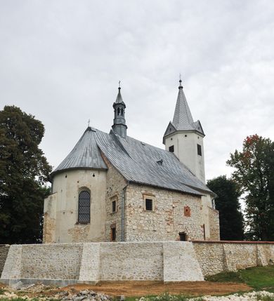 Zdjęcie nr 11: Kościół położony jest na wzniesieniu, obwiedziony dookoła niskim murem. Świątynia murowana, orientowana, jednonawowa na planie prostokątnej nawy z węższym prezbiterium zamkniętym półkoliście, z wieżą od zachodu; przykryty wysokim dwuspadowym dachem, z sygnaturką nad prezbiterium. Wieża czworoboczna, w przyziemiu mieszcząca kruchtę, wyżej przechodząca w ośmiobok, zwieńczona stylizowanym na gotycki, iglicowym, pokrytym blachą hełmem, flankowanym trójkątnymi szczycikami. Od południa kościoła usytuowana jest druga kruchta z kamiennym portalem, a od północy zakrystia z dodatkowym pomieszczeniem na paramenty liturgiczne, nad nimi empora. Prezbiterium oraz nawę obejmuje z zewnątrz sześć wysokich skarp. Wewnątrz podziały architektoniczne wydzielają przyścienne filary w nawie z silnie wysuniętym do wnętrza łukiem tęczy. Prezbiterium oraz nawę oświetla pięć wysokich okien, zamkniętych półkoliście, usytuowanych od południa. Portal główny wykonany z wapienia pińczowskiego o typie arkadowym z charakterystycznym układem kamiennych ciosów dźwiga boniowany łuk archiwolty. Nad nim trójkątny przyczółek, silnie wysunięty przed lico ściany, ujęty dookoła wydatnym, profilowanym gzymsem z kartuszem w polu z herbami: Lubicz, Leliwa, Junosza i Rawicz oraz inicjałami „ALDL” i datą „An[n]o D[omi]ni 1623”. Portal południowy z wapienia jurajskiego o wykroju zbliżonym do ostrołukowego (krzywo wycięty). Natomiast portal do zakrystii o renesansowej budowie i dekoracji. Nawa sklepiona krzyżowo-kolebkowo.
Do zewnętrznej, południowej ściany kościoła dostawiony jest pomnik nagrobny hrabiego Jakuba z Granowa i Eleonory z Dembowskich Wodzickich.