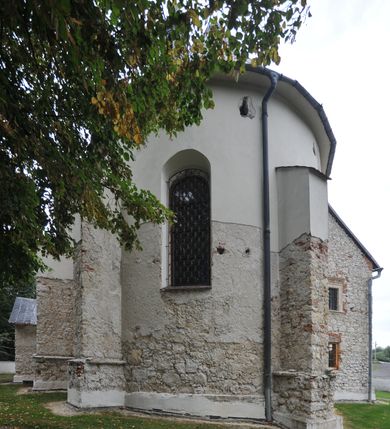 Zdjęcie nr 13: Kościół położony jest na wzniesieniu, obwiedziony dookoła niskim murem. Świątynia murowana, orientowana, jednonawowa na planie prostokątnej nawy z węższym prezbiterium zamkniętym półkoliście, z wieżą od zachodu; przykryty wysokim dwuspadowym dachem, z sygnaturką nad prezbiterium. Wieża czworoboczna, w przyziemiu mieszcząca kruchtę, wyżej przechodząca w ośmiobok, zwieńczona stylizowanym na gotycki, iglicowym, pokrytym blachą hełmem, flankowanym trójkątnymi szczycikami. Od południa kościoła usytuowana jest druga kruchta z kamiennym portalem, a od północy zakrystia z dodatkowym pomieszczeniem na paramenty liturgiczne, nad nimi empora. Prezbiterium oraz nawę obejmuje z zewnątrz sześć wysokich skarp. Wewnątrz podziały architektoniczne wydzielają przyścienne filary w nawie z silnie wysuniętym do wnętrza łukiem tęczy. Prezbiterium oraz nawę oświetla pięć wysokich okien, zamkniętych półkoliście, usytuowanych od południa. Portal główny wykonany z wapienia pińczowskiego o typie arkadowym z charakterystycznym układem kamiennych ciosów dźwiga boniowany łuk archiwolty. Nad nim trójkątny przyczółek, silnie wysunięty przed lico ściany, ujęty dookoła wydatnym, profilowanym gzymsem z kartuszem w polu z herbami: Lubicz, Leliwa, Junosza i Rawicz oraz inicjałami „ALDL” i datą „An[n]o D[omi]ni 1623”. Portal południowy z wapienia jurajskiego o wykroju zbliżonym do ostrołukowego (krzywo wycięty). Natomiast portal do zakrystii o renesansowej budowie i dekoracji. Nawa sklepiona krzyżowo-kolebkowo.
Do zewnętrznej, południowej ściany kościoła dostawiony jest pomnik nagrobny hrabiego Jakuba z Granowa i Eleonory z Dembowskich Wodzickich.