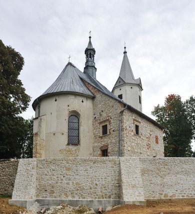 Zdjęcie nr 12: Kościół położony jest na wzniesieniu, obwiedziony dookoła niskim murem. Świątynia murowana, orientowana, jednonawowa na planie prostokątnej nawy z węższym prezbiterium zamkniętym półkoliście, z wieżą od zachodu; przykryty wysokim dwuspadowym dachem, z sygnaturką nad prezbiterium. Wieża czworoboczna, w przyziemiu mieszcząca kruchtę, wyżej przechodząca w ośmiobok, zwieńczona stylizowanym na gotycki, iglicowym, pokrytym blachą hełmem, flankowanym trójkątnymi szczycikami. Od południa kościoła usytuowana jest druga kruchta z kamiennym portalem, a od północy zakrystia z dodatkowym pomieszczeniem na paramenty liturgiczne, nad nimi empora. Prezbiterium oraz nawę obejmuje z zewnątrz sześć wysokich skarp. Wewnątrz podziały architektoniczne wydzielają przyścienne filary w nawie z silnie wysuniętym do wnętrza łukiem tęczy. Prezbiterium oraz nawę oświetla pięć wysokich okien, zamkniętych półkoliście, usytuowanych od południa. Portal główny wykonany z wapienia pińczowskiego o typie arkadowym z charakterystycznym układem kamiennych ciosów dźwiga boniowany łuk archiwolty. Nad nim trójkątny przyczółek, silnie wysunięty przed lico ściany, ujęty dookoła wydatnym, profilowanym gzymsem z kartuszem w polu z herbami: Lubicz, Leliwa, Junosza i Rawicz oraz inicjałami „ALDL” i datą „An[n]o D[omi]ni 1623”. Portal południowy z wapienia jurajskiego o wykroju zbliżonym do ostrołukowego (krzywo wycięty). Natomiast portal do zakrystii o renesansowej budowie i dekoracji. Nawa sklepiona krzyżowo-kolebkowo.
Do zewnętrznej, południowej ściany kościoła dostawiony jest pomnik nagrobny hrabiego Jakuba z Granowa i Eleonory z Dembowskich Wodzickich.