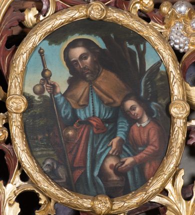 Zdjęcie nr 1: Obraz w kształcie owalu z przedstawieniem św. Rocha. W centrum kompozycji ukazany święty w trzech czwartych wysokości, zwrócony delikatnie w prawo z lewą dłonią odsłaniającą ranę na lewej nodze, z laską pielgrzyma i bukłakiem w prawej ręce. Twarz podłużna, nos długi i wąski, oczy ciemne, półkoliste łuki brwiowe, broda krótka i delikatnie siwa. Włosy długie, bujne, spływające na plecy; wokół głowy, kolisty i złoty nimb. Święty jest ubrany w niebieską suknię z długimi rękawami, przewiązaną w talii paskiem, zapiętą w górnej części na rząd guziczków, brązową narzutkę na ramiona oraz czerwony płaszcz widoczny z prawego boku, przewieszony przez pasek, u którego również zawieszony mały bukłak na wodę. Po prawej stronie obrazu znajduje się anioł ocierający ranę na nodze św. Rocha. Anioł o niskim wzroście, ubrany w czerwoną sukienkę z białym kołnierzykiem. Po lewej stronie obrazu pies. W tle widoczny pejzaż i wysokie drzewa oraz błękitne niebo. Kolorystyka przygaszona. Rama złocona w formie wieńca z liści wawrzynu zdobiona czterema małymi różami.
