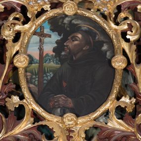 Zdjęcie nr 1: Obraz w kształcie owalu z przedstawieniem św. Franciszka z Asyżu. W centrum kompozycji święty ukazany w półpostaci, zwrócony delikatnie w prawo z dłońmi splecionymi i złożonymi na znajdującej się w dolnej części obrazu czaszce, głowa delikatnie uniesiona. Twarz podłużna, widoczna z lewego profilu, nos długi spiczasty, oczy ciemne i przymknięte, półkoliste łuki brwiowe, broda krótka i siwa. Na głowie tonsura, nad nią okrągły i złoty nimb. Święty jest ubrany w brązowy habit franciszkański. Na dłoniach oraz boku ma ślady po stygmatach. Po lewej stronie obrazu znajduje się krucyfiks. Krzyż brązowy i prosty. Chrystus rozpięty na wyprężonych ramionach, przybity do krzyża trzema gwoździami. Sylwetka szczupła, o ciemnej karnacji. Przewiązany jest w pasie białym perizonium, zawiązanym na prawym boku. Wokół głowy ma złoty i okrągły nimb. Nad nią wisi biały titulus w formie banderoli. W tle widoczny pejzaż z zabudowaniami oraz błękitno-różowe niebo, po prawej stronie obrazu ciemna szczelina skalna. Kolorystyka przygaszona. Rama złocona w formie wieńca z liści wawrzynu zdobiona czterema małymi różami.


