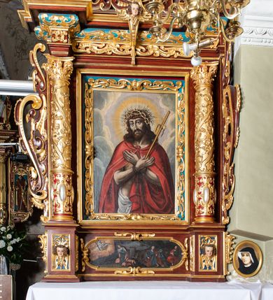 Zdjęcie nr 4: Ołtarz architektoniczny, jednoosiowy, jednokondygnacyjny ze zwieńczeniem. Ołtarz murowany, prostopadłościenny z kamienną mensą. Antepedium drewniane, w polu którego ozdobny, płaskorzeźbiony monogram Chrystusa na niebieskim tle wraz z dekoracją ornamentalną w narożach pola. Pole ujęte ozdobną ramą z płaskorzeźbionym ornamentem z wici roślinnej na jasnoniebieskim tle. Drewniane retabulum ustawione na cokole. W polu obraz z przedstawieniem Modlitwy w Ogrójcu w kształcie leżącego prostokąta o krótszych bokach zakończonych łukiem nadwieszonym. Nastawa flankowana parą kolumn podtrzymujących wyłamane nad osią główną belkowanie. W polu głównym obraz Ecce Homo, a na zasuwie obraz św. Antoniego Padewskiego. Zwieńczenie w formie owalu ujętego ażurową dekoracją formowaną z ornamentu małżowinowo-chrząstkowego na tle kwadratowej ramy. W polu obraz Chrystusa u słupa, po bokach figury, po lewej św. Mikołaja, po prawej św. Doroty, na szczycie figura św. Józefa. Partie cokołów ozdobione płycinami z uskrzydlonymi główkami aniołów w polu, po bokach dekorowane ornamentem małżowinowo-chrząstkowym. Zasadnicza część nastawy ujęta po bokach uszami z ornamentem o formach małżowinowo-chrząstkowych, z czego prawy złożony, dostosowany do południowego filaru kościoła. Trzony kolumn w dolnej partii ozdobione kartuszami o fantazyjnych wycięciach z motywami kaboszonów, w górnej partii pokryte dekoracją w formie wici winnej latorośli. W partii fryzu oraz pod gzymsem ornamentyka roślinna. Pośrodku belkowania motyw dekoracyjnego spływu z uskrzydloną główką aniołka z podwiązaną chustą pod szyją. Pole środkowe w formie prostokątnej wnęki ujętej profilowanymi ramami z czego wewnętrzna ozdobiona ornamentem małżowinowo-chrząstkowym. Polichromia struktury ołtarza utrzymana w odcieniach ciemnego brązu i czerwieni, partie w tle ornamentów niebieskie. Ornamentyka i elementy detalu architektonicznego złocone i srebrzone. 

