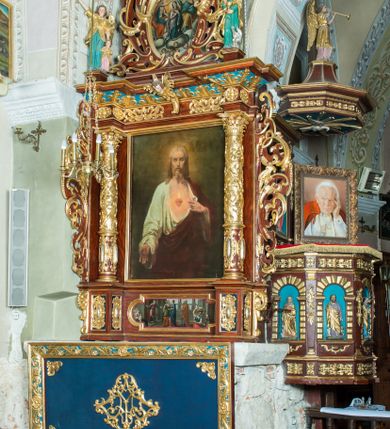Zdjęcie nr 13: Ołtarz architektoniczny, jednoosiowy, jednokondygnacyjny ze zwieńczeniem. Ołtarz murowany, prostopadłościenny z kamienną mensą. Antepedium drewniane, w polu którego ozdobny, płaskorzeźbiony monogram maryjny na niebieskim tle oraz dekoracja ornamentalna w narożach pola. Pole ujęte ozdobną ramą z płaskorzeźbionym ornamentem z wici roślinnej na jasnoniebieskim tle. Drewniane retabulum ustawione na cokole. W predelli obraz z przedstawieniem Nawiedzenia Najświętszej Marii Panny w kształcie leżącego prostokąta o krótszych bokach zakończonych półkolistym łukiem nadwieszonym. Nastawa flankowana parą kolumn podtrzymujących wyłamane nad osią główną belkowanie. W polu głównym obraz Matki Boskiej Śnieżnej, a na zasuwie obraz Najświętsze Serce Jezusa. Zwieńczenie w formie owalu ujętego dekoracyjną, ażurową ramą formowaną z ornamentu małżowinowo-chrząstkowego na tle kwadratowej ramy. W polu znajduje się obraz „Koronacja Najświętszej Marii Panny”, a po bokach figury, po lewej: św. Archanioła Rafała z Tobiaszem, po prawej: św. Jana Ewangelisty, na szczycie figura św. Michała Archanioła. Partie cokołów ozdobione są ornamentem w formie kartusza o fantazyjnie kształtowanych krawędziach, z motywem kaboszonów pośrodku. Cokoły po zewnętrznej stronie zostały ozdobione ornamentalnym podwieszeniem z motywem małżowinowo-chrząstkowym. Zasadnicza część nastawy ujęta po bokach uszami z ornamentem o formach małżowinowo-chrząstkowych, z czego lewy złożony, dostosowany do północnego filaru kościoła. Trzony kolumn w dolnej partii ozdobione kartuszami o fantazyjnych wycięciach z motywami kaboszonów, w górnej partii pokryte dekoracją w formie wici winnej latorośli. W partii fryzu oraz pod gzymsem ornamentyka roślinna. Pośrodku belkowania motyw dekoracyjnego spływu z uskrzydloną główką aniołka z podwiązaną chustą pod szyją. Pole środkowe w formie prostokątnej wnęki ujętej profilowanymi ramami z czego wewnętrzna ozdobiona ornamentem małżowinowo-chrząstkowym z motywami uskrzydlonych główek aniołków pośrodku każdego boku ramy. Polichromia struktury ołtarza utrzymana w odcieniach ciemnego brązu i bordo, partie w tle ornamentów niebieskie. Ornamentyka i elementy detalu architektonicznego złocone i srebrzone. 