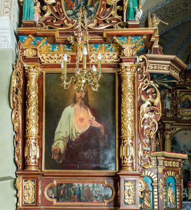 Zdjęcie nr 11: Ołtarz architektoniczny, jednoosiowy, jednokondygnacyjny ze zwieńczeniem. Ołtarz murowany, prostopadłościenny z kamienną mensą. Antepedium drewniane, w polu którego ozdobny, płaskorzeźbiony monogram maryjny na niebieskim tle oraz dekoracja ornamentalna w narożach pola. Pole ujęte ozdobną ramą z płaskorzeźbionym ornamentem z wici roślinnej na jasnoniebieskim tle. Drewniane retabulum ustawione na cokole. W predelli obraz z przedstawieniem Nawiedzenia Najświętszej Marii Panny w kształcie leżącego prostokąta o krótszych bokach zakończonych półkolistym łukiem nadwieszonym. Nastawa flankowana parą kolumn podtrzymujących wyłamane nad osią główną belkowanie. W polu głównym obraz Matki Boskiej Śnieżnej, a na zasuwie obraz Najświętsze Serce Jezusa. Zwieńczenie w formie owalu ujętego dekoracyjną, ażurową ramą formowaną z ornamentu małżowinowo-chrząstkowego na tle kwadratowej ramy. W polu znajduje się obraz „Koronacja Najświętszej Marii Panny”, a po bokach figury, po lewej: św. Archanioła Rafała z Tobiaszem, po prawej: św. Jana Ewangelisty, na szczycie figura św. Michała Archanioła. Partie cokołów ozdobione są ornamentem w formie kartusza o fantazyjnie kształtowanych krawędziach, z motywem kaboszonów pośrodku. Cokoły po zewnętrznej stronie zostały ozdobione ornamentalnym podwieszeniem z motywem małżowinowo-chrząstkowym. Zasadnicza część nastawy ujęta po bokach uszami z ornamentem o formach małżowinowo-chrząstkowych, z czego lewy złożony, dostosowany do północnego filaru kościoła. Trzony kolumn w dolnej partii ozdobione kartuszami o fantazyjnych wycięciach z motywami kaboszonów, w górnej partii pokryte dekoracją w formie wici winnej latorośli. W partii fryzu oraz pod gzymsem ornamentyka roślinna. Pośrodku belkowania motyw dekoracyjnego spływu z uskrzydloną główką aniołka z podwiązaną chustą pod szyją. Pole środkowe w formie prostokątnej wnęki ujętej profilowanymi ramami z czego wewnętrzna ozdobiona ornamentem małżowinowo-chrząstkowym z motywami uskrzydlonych główek aniołków pośrodku każdego boku ramy. Polichromia struktury ołtarza utrzymana w odcieniach ciemnego brązu i bordo, partie w tle ornamentów niebieskie. Ornamentyka i elementy detalu architektonicznego złocone i srebrzone. 