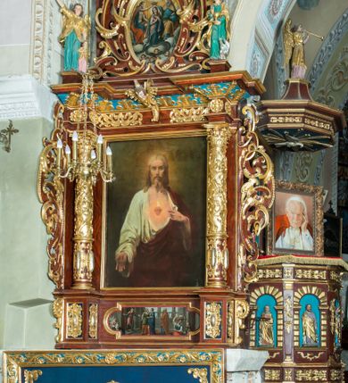 Zdjęcie nr 14: Ołtarz architektoniczny, jednoosiowy, jednokondygnacyjny ze zwieńczeniem. Ołtarz murowany, prostopadłościenny z kamienną mensą. Antepedium drewniane, w polu którego ozdobny, płaskorzeźbiony monogram maryjny na niebieskim tle oraz dekoracja ornamentalna w narożach pola. Pole ujęte ozdobną ramą z płaskorzeźbionym ornamentem z wici roślinnej na jasnoniebieskim tle. Drewniane retabulum ustawione na cokole. W predelli obraz z przedstawieniem Nawiedzenia Najświętszej Marii Panny w kształcie leżącego prostokąta o krótszych bokach zakończonych półkolistym łukiem nadwieszonym. Nastawa flankowana parą kolumn podtrzymujących wyłamane nad osią główną belkowanie. W polu głównym obraz Matki Boskiej Śnieżnej, a na zasuwie obraz Najświętsze Serce Jezusa. Zwieńczenie w formie owalu ujętego dekoracyjną, ażurową ramą formowaną z ornamentu małżowinowo-chrząstkowego na tle kwadratowej ramy. W polu znajduje się obraz „Koronacja Najświętszej Marii Panny”, a po bokach figury, po lewej: św. Archanioła Rafała z Tobiaszem, po prawej: św. Jana Ewangelisty, na szczycie figura św. Michała Archanioła. Partie cokołów ozdobione są ornamentem w formie kartusza o fantazyjnie kształtowanych krawędziach, z motywem kaboszonów pośrodku. Cokoły po zewnętrznej stronie zostały ozdobione ornamentalnym podwieszeniem z motywem małżowinowo-chrząstkowym. Zasadnicza część nastawy ujęta po bokach uszami z ornamentem o formach małżowinowo-chrząstkowych, z czego lewy złożony, dostosowany do północnego filaru kościoła. Trzony kolumn w dolnej partii ozdobione kartuszami o fantazyjnych wycięciach z motywami kaboszonów, w górnej partii pokryte dekoracją w formie wici winnej latorośli. W partii fryzu oraz pod gzymsem ornamentyka roślinna. Pośrodku belkowania motyw dekoracyjnego spływu z uskrzydloną główką aniołka z podwiązaną chustą pod szyją. Pole środkowe w formie prostokątnej wnęki ujętej profilowanymi ramami z czego wewnętrzna ozdobiona ornamentem małżowinowo-chrząstkowym z motywami uskrzydlonych główek aniołków pośrodku każdego boku ramy. Polichromia struktury ołtarza utrzymana w odcieniach ciemnego brązu i bordo, partie w tle ornamentów niebieskie. Ornamentyka i elementy detalu architektonicznego złocone i srebrzone. 