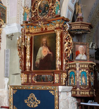 Zdjęcie nr 1: Ołtarz architektoniczny, jednoosiowy, jednokondygnacyjny ze zwieńczeniem. Ołtarz murowany, prostopadłościenny z kamienną mensą. Antepedium drewniane, w polu którego ozdobny, płaskorzeźbiony monogram maryjny na niebieskim tle oraz dekoracja ornamentalna w narożach pola. Pole ujęte ozdobną ramą z płaskorzeźbionym ornamentem z wici roślinnej na jasnoniebieskim tle. Drewniane retabulum ustawione na cokole. W predelli obraz z przedstawieniem Nawiedzenia Najświętszej Marii Panny w kształcie leżącego prostokąta o krótszych bokach zakończonych półkolistym łukiem nadwieszonym. Nastawa flankowana parą kolumn podtrzymujących wyłamane nad osią główną belkowanie. W polu głównym obraz Matki Boskiej Śnieżnej, a na zasuwie obraz Najświętsze Serce Jezusa. Zwieńczenie w formie owalu ujętego dekoracyjną, ażurową ramą formowaną z ornamentu małżowinowo-chrząstkowego na tle kwadratowej ramy. W polu znajduje się obraz „Koronacja Najświętszej Marii Panny”, a po bokach figury, po lewej: św. Archanioła Rafała z Tobiaszem, po prawej: św. Jana Ewangelisty, na szczycie figura św. Michała Archanioła. Partie cokołów ozdobione są ornamentem w formie kartusza o fantazyjnie kształtowanych krawędziach, z motywem kaboszonów pośrodku. Cokoły po zewnętrznej stronie zostały ozdobione ornamentalnym podwieszeniem z motywem małżowinowo-chrząstkowym. Zasadnicza część nastawy ujęta po bokach uszami z ornamentem o formach małżowinowo-chrząstkowych, z czego lewy złożony, dostosowany do północnego filaru kościoła. Trzony kolumn w dolnej partii ozdobione kartuszami o fantazyjnych wycięciach z motywami kaboszonów, w górnej partii pokryte dekoracją w formie wici winnej latorośli. W partii fryzu oraz pod gzymsem ornamentyka roślinna. Pośrodku belkowania motyw dekoracyjnego spływu z uskrzydloną główką aniołka z podwiązaną chustą pod szyją. Pole środkowe w formie prostokątnej wnęki ujętej profilowanymi ramami z czego wewnętrzna ozdobiona ornamentem małżowinowo-chrząstkowym z motywami uskrzydlonych główek aniołków pośrodku każdego boku ramy. Polichromia struktury ołtarza utrzymana w odcieniach ciemnego brązu i bordo, partie w tle ornamentów niebieskie. Ornamentyka i elementy detalu architektonicznego złocone i srebrzone. 