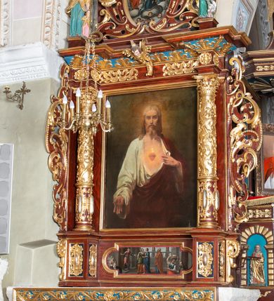 Zdjęcie nr 15: Ołtarz architektoniczny, jednoosiowy, jednokondygnacyjny ze zwieńczeniem. Ołtarz murowany, prostopadłościenny z kamienną mensą. Antepedium drewniane, w polu którego ozdobny, płaskorzeźbiony monogram maryjny na niebieskim tle oraz dekoracja ornamentalna w narożach pola. Pole ujęte ozdobną ramą z płaskorzeźbionym ornamentem z wici roślinnej na jasnoniebieskim tle. Drewniane retabulum ustawione na cokole. W predelli obraz z przedstawieniem Nawiedzenia Najświętszej Marii Panny w kształcie leżącego prostokąta o krótszych bokach zakończonych półkolistym łukiem nadwieszonym. Nastawa flankowana parą kolumn podtrzymujących wyłamane nad osią główną belkowanie. W polu głównym obraz Matki Boskiej Śnieżnej, a na zasuwie obraz Najświętsze Serce Jezusa. Zwieńczenie w formie owalu ujętego dekoracyjną, ażurową ramą formowaną z ornamentu małżowinowo-chrząstkowego na tle kwadratowej ramy. W polu znajduje się obraz „Koronacja Najświętszej Marii Panny”, a po bokach figury, po lewej: św. Archanioła Rafała z Tobiaszem, po prawej: św. Jana Ewangelisty, na szczycie figura św. Michała Archanioła. Partie cokołów ozdobione są ornamentem w formie kartusza o fantazyjnie kształtowanych krawędziach, z motywem kaboszonów pośrodku. Cokoły po zewnętrznej stronie zostały ozdobione ornamentalnym podwieszeniem z motywem małżowinowo-chrząstkowym. Zasadnicza część nastawy ujęta po bokach uszami z ornamentem o formach małżowinowo-chrząstkowych, z czego lewy złożony, dostosowany do północnego filaru kościoła. Trzony kolumn w dolnej partii ozdobione kartuszami o fantazyjnych wycięciach z motywami kaboszonów, w górnej partii pokryte dekoracją w formie wici winnej latorośli. W partii fryzu oraz pod gzymsem ornamentyka roślinna. Pośrodku belkowania motyw dekoracyjnego spływu z uskrzydloną główką aniołka z podwiązaną chustą pod szyją. Pole środkowe w formie prostokątnej wnęki ujętej profilowanymi ramami z czego wewnętrzna ozdobiona ornamentem małżowinowo-chrząstkowym z motywami uskrzydlonych główek aniołków pośrodku każdego boku ramy. Polichromia struktury ołtarza utrzymana w odcieniach ciemnego brązu i bordo, partie w tle ornamentów niebieskie. Ornamentyka i elementy detalu architektonicznego złocone i srebrzone. 