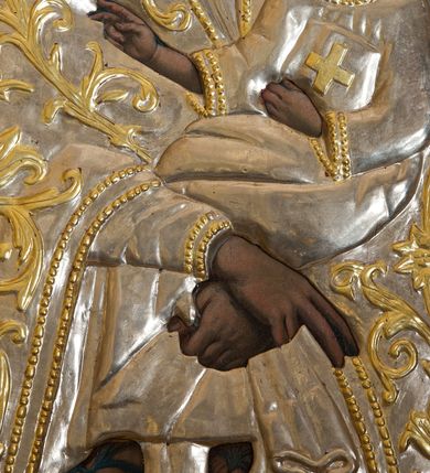 Zdjęcie nr 4: Obraz w kształcie stojącego prostokąta z wizerunkiem Matki Boskiej Śnieżnej. Maria przedstawiona frontalnie, w półpostaci, z Dzieciątkiem Jezus na lewym ręku, ze skrzyżowanymi dłońmi. Twarz podłużna, z długim i wąskim nosem, drobnymi ustami, dużymi oczami obwiedzionymi regularnymi łukami brwiowymi, ze wzrokiem skierowanym wprost na widza. Dzieciątko zwrócone trzy czwarte w prawo, w pozycji siedzącej, z książką ze znakiem krzyża na obwolucie w lewej dłoni, prawą czyniące gest błogosławieństwa, na stopach ma namalowane rzymskie sandałki. Twarz okrągła o wyrazistych rysach, duże i brązowe oczy, zarumienione policzki, włosy kręcone, średniej długości opadające na plecy, wzrok skierowany na Matkę. Wokół głów Marii i Dzieciątka złote i koliste nimby. Tło w ciemnych odcieniach szarości i koloru niebieskiego, rozjaśnione w górnej części. Na postacie Marii i Dzieciątka nałożone metalowe: sukienki, korony w typie zamkniętym oraz chustka w dłoni Marii. Sukienki ozdobione wicią roślinną z kwiatami.




