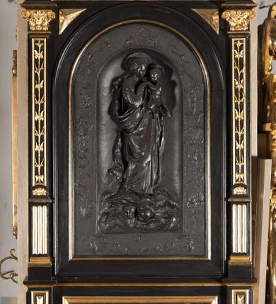 Zdjęcie nr 1: Płaskorzeźba przedstawiająca Matkę Boską z Dzieciątkiem w bogatym obramieniu w formie aediculi. Maria została przedstawiona całopostaciowo, zwrócona w trzech czwartych w lewo, z lewą nogą wysuniętą do przodu. Ma młodą twarz, którą okalają długie, opadające na plecy włosy. Jest ubrana w długą suknię i płaszcz, który tworzy obszerny zawój wokół jej prawego biodra. Lewą ręką podtrzymuje Dzieciątko, do którego wyciąga prawą rękę. Dzieciątko jest nagie, patrzy na Marię, wyciąga dłoń do jej ręki. Postacie stoją na obłokach, w których unoszą się główki anielskie. Intymne wyobrażenie jest ujęte bordiurą ze scenami z życia Marii. Płaskorzeźba ma kształt stojącego prostokąta zamkniętego od góry łukiem półkolistym. Ujmują ją pilastry o dekorowanych trzonach oparte na szerokim cokole z płyciną z napisem „ŚWIĘTA BOŻA RODZICIELKO / MÓDL SIĘ ZA NAMI”. Na dole cokołu podwieszenie z kartuszem z inskrypcją „DZIEŁO DŁUTA / TEOFILA LENARTOWICZA / DAR HRABIANKI / HELENY MAŁACHOWSKIEJ”. Od góry kompozycję zamyka trójkątny, przerwany przyczółek z kartuszem herbowym. Obramienie polichromowane na kolor czarny, profile, ornamenty i detale złocone. 