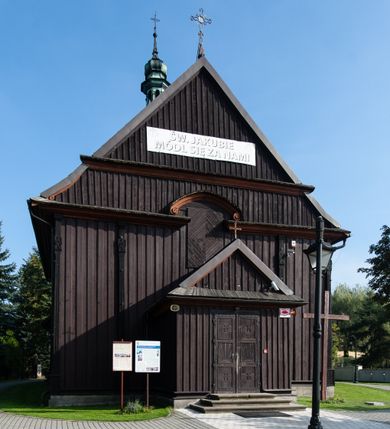 Zdjęcie nr 6: Kościół orientowany, jednonawowy, z węższym, zamkniętym wielobocznie prezbiterium, przy którym od północy prostokątna zakrystia (obecnie skarbiec) od południa prostokątna nowa zakrystia. Przy korpusie od południa i zachodu kruchty. Wewnątrz stropy, w prezbiterium i środkowej części nawy z fasetami; w nawie boczne płaskie odcinki stropu wparte na dwóch słupach. W prezbiterium i nawie na stropach dekoracja geometryczna z listew. Ściany artykułowane pilastrami. Tęcza o wystroju prostokątnym, ujęta przyściennymi filarami. Zewnątrz ściany szalowane deskowaniem na nakładkę, opięte pilastrami. Fasada rozczłonkowana czterema pilastrami wspierającymi gzyms, pośrodku wyłamany nad oknem wchodzącym w pole szczytu. Szczyt trójkątny, w połowie przedzielony gzymsem. Dachy dwuspadowe, nad prezbiterium wielopołaciowy, nad nową zakrystią namiotowy oraz pulpitowe; na kalenicy dachu nawy sygnaturka. Okna prostokątne w profilowanych obramieniach. Portal uszaty, z datą: 1748.