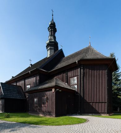 Zdjęcie nr 7: Kościół orientowany, jednonawowy, z węższym, zamkniętym wielobocznie prezbiterium, przy którym od północy prostokątna zakrystia (obecnie skarbiec) od południa prostokątna nowa zakrystia. Przy korpusie od południa i zachodu kruchty. Wewnątrz stropy, w prezbiterium i środkowej części nawy z fasetami; w nawie boczne płaskie odcinki stropu wparte na dwóch słupach. W prezbiterium i nawie na stropach dekoracja geometryczna z listew. Ściany artykułowane pilastrami. Tęcza o wystroju prostokątnym, ujęta przyściennymi filarami. Zewnątrz ściany szalowane deskowaniem na nakładkę, opięte pilastrami. Fasada rozczłonkowana czterema pilastrami wspierającymi gzyms, pośrodku wyłamany nad oknem wchodzącym w pole szczytu. Szczyt trójkątny, w połowie przedzielony gzymsem. Dachy dwuspadowe, nad prezbiterium wielopołaciowy, nad nową zakrystią namiotowy oraz pulpitowe; na kalenicy dachu nawy sygnaturka. Okna prostokątne w profilowanych obramieniach. Portal uszaty, z datą: 1748.