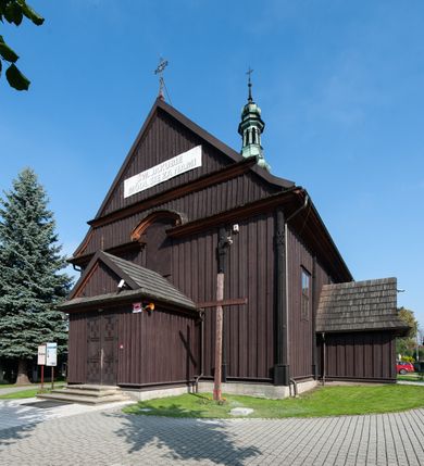 Zdjęcie nr 9: Kościół orientowany, jednonawowy, z węższym, zamkniętym wielobocznie prezbiterium, przy którym od północy prostokątna zakrystia (obecnie skarbiec) od południa prostokątna nowa zakrystia. Przy korpusie od południa i zachodu kruchty. Wewnątrz stropy, w prezbiterium i środkowej części nawy z fasetami; w nawie boczne płaskie odcinki stropu wparte na dwóch słupach. W prezbiterium i nawie na stropach dekoracja geometryczna z listew. Ściany artykułowane pilastrami. Tęcza o wystroju prostokątnym, ujęta przyściennymi filarami. Zewnątrz ściany szalowane deskowaniem na nakładkę, opięte pilastrami. Fasada rozczłonkowana czterema pilastrami wspierającymi gzyms, pośrodku wyłamany nad oknem wchodzącym w pole szczytu. Szczyt trójkątny, w połowie przedzielony gzymsem. Dachy dwuspadowe, nad prezbiterium wielopołaciowy, nad nową zakrystią namiotowy oraz pulpitowe; na kalenicy dachu nawy sygnaturka. Okna prostokątne w profilowanych obramieniach. Portal uszaty, z datą: 1748.